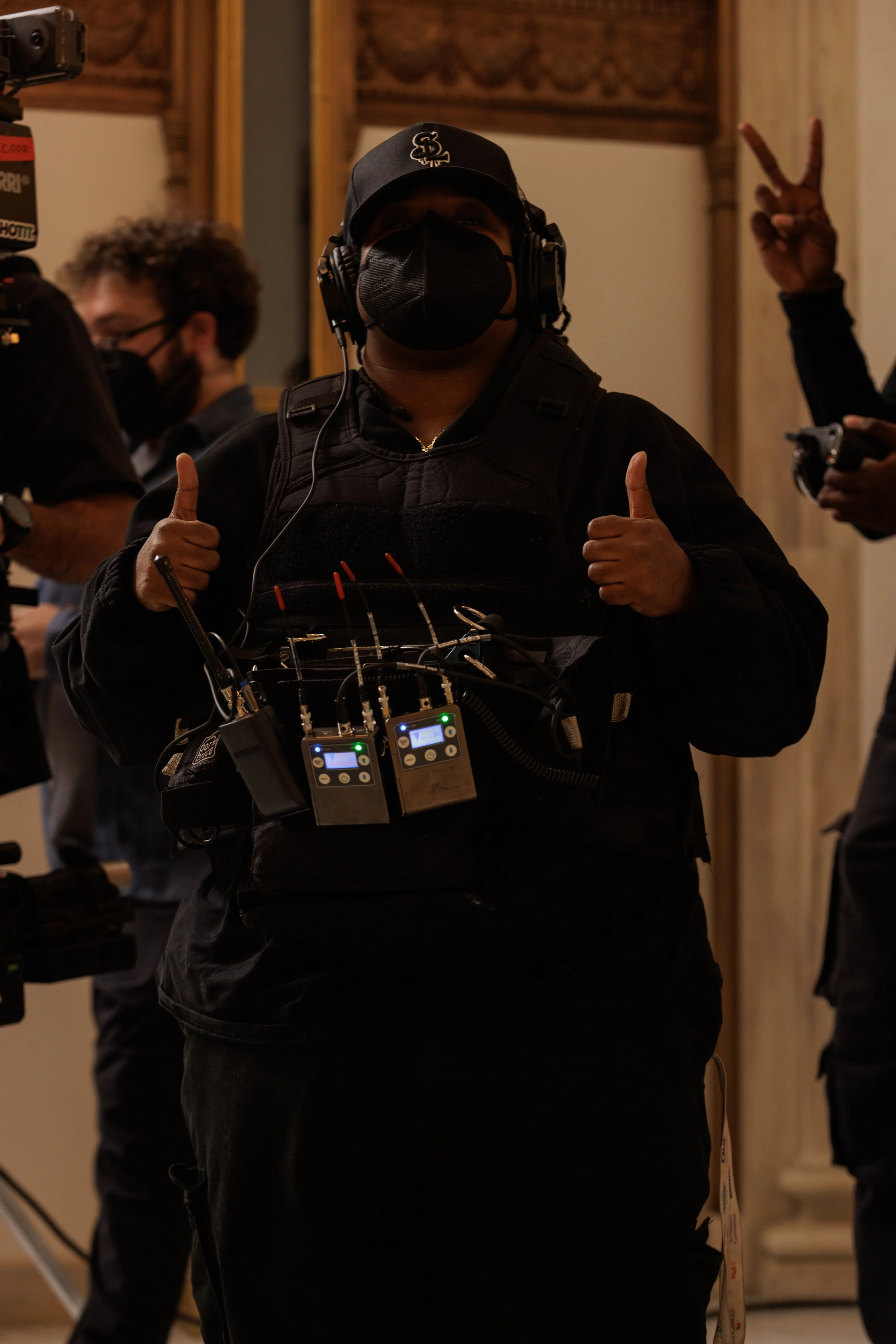 Person wearing headphones, face mask, and wheeled communication equipment, giving a thumbs-up.