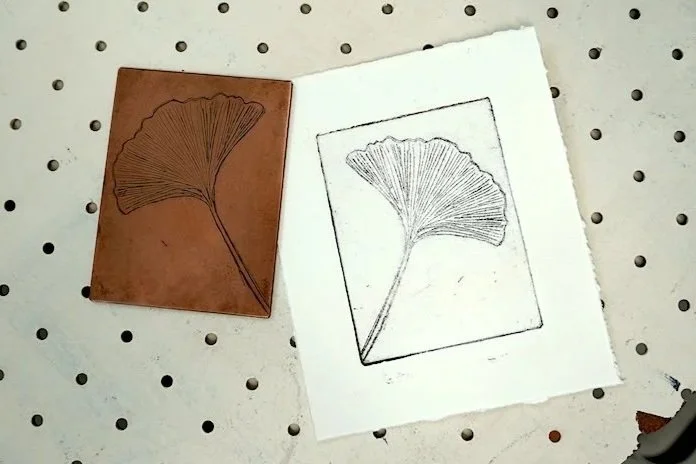 A copper plate etched with a gingko leaf next to the print made with the same image. This print was made in Groundworks Art Lab's Copper Etching printmaking class in Boulder, CO