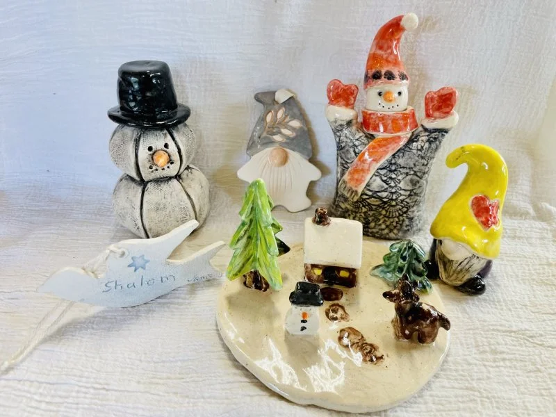 A collection of handmade ceramic winter holiday decorations such as snowmen, gnomes, and a winter village made at Groundworks Art Lab in Boulder, CO