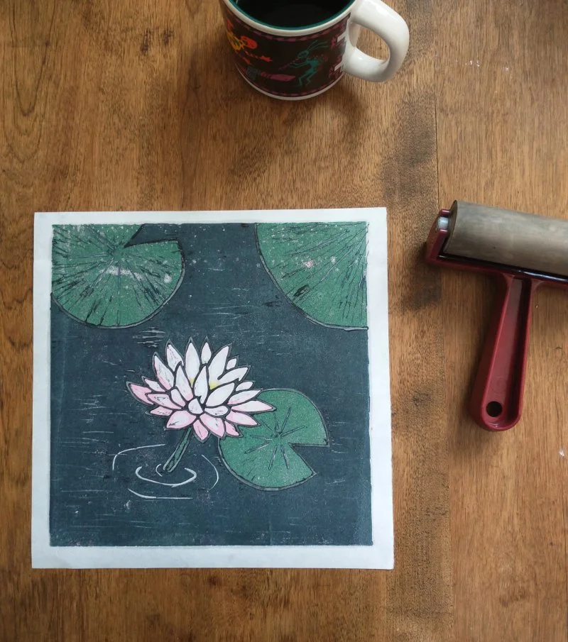 A linocut of a lotus blossom and lily pads next to a brayer. Learn reduction printing in Level II Linocut at Groundworks Art Lab in Boulder, CO.
