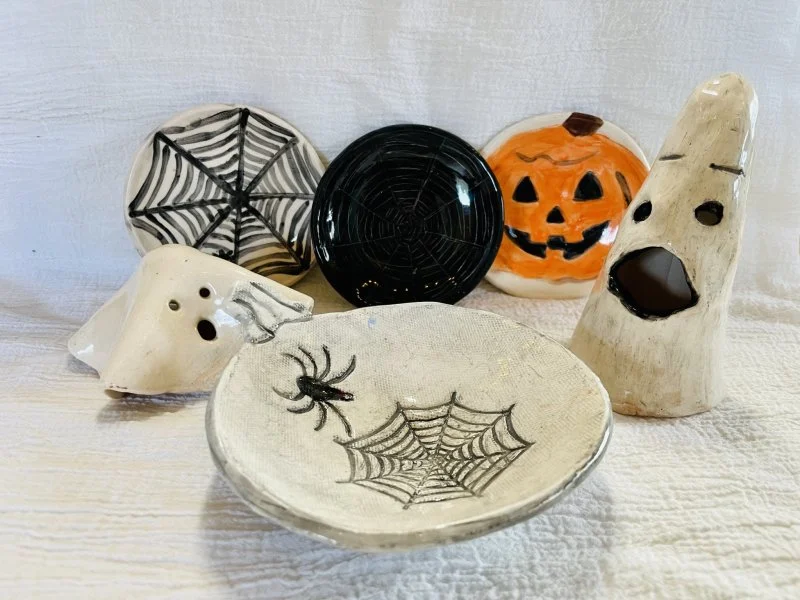 A collection of handmade ceramic Halloween decorations such as ghosts, jack-o-lanterns, and spiderweb dishes made at Groundworks Art Lab in Boulder, CO
