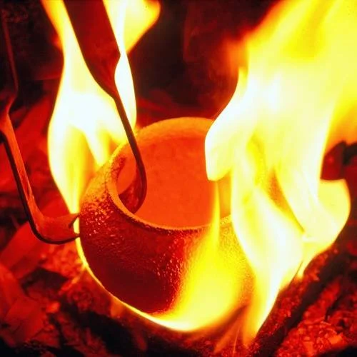 Photo of tongs pulling a piece of pottery out of an open flame during a raku firing. Raku is one of the firings taught in clay classes at Groundworks Art Lab in Boulder, CO