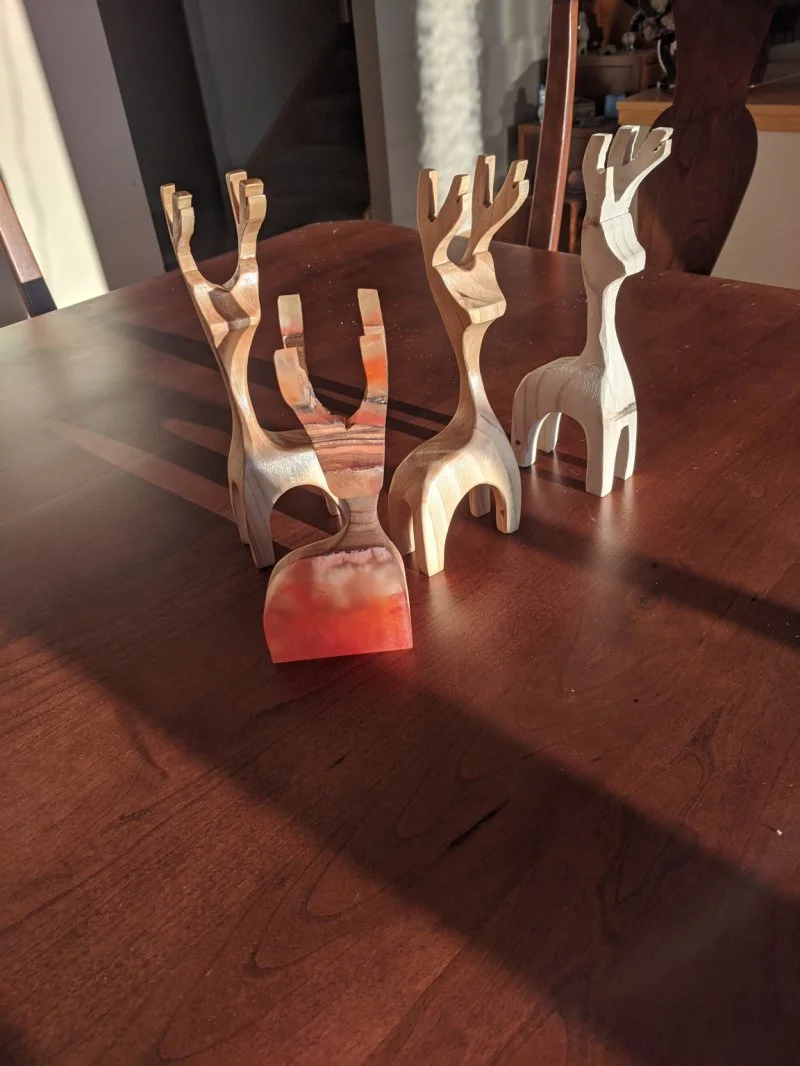 Small hand-carved wooden deer figurines on a table. These are examples of the carvings made in the Grain & Glow Adult Summer Camp at Groundworks Art Lab in Boulder, CO