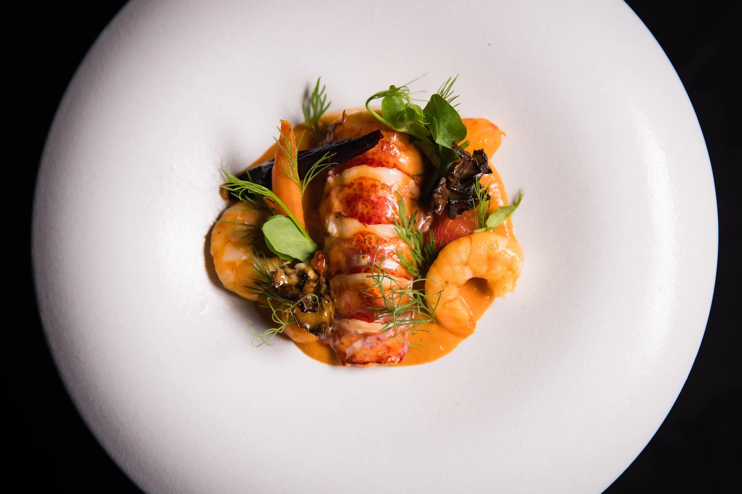Elegant seafood dish with shrimp, lobster, and garnishes on a white plate.