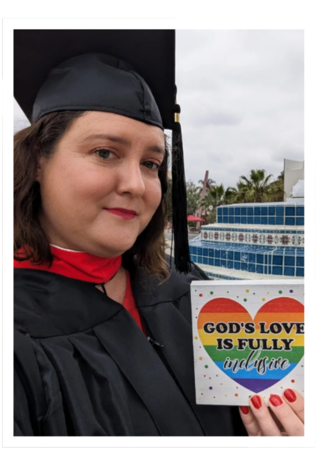 Amanda Pence in a graduation cap and gown holding a colorful card with a rainbow heart and the message 'God's love is fully inclusive'.