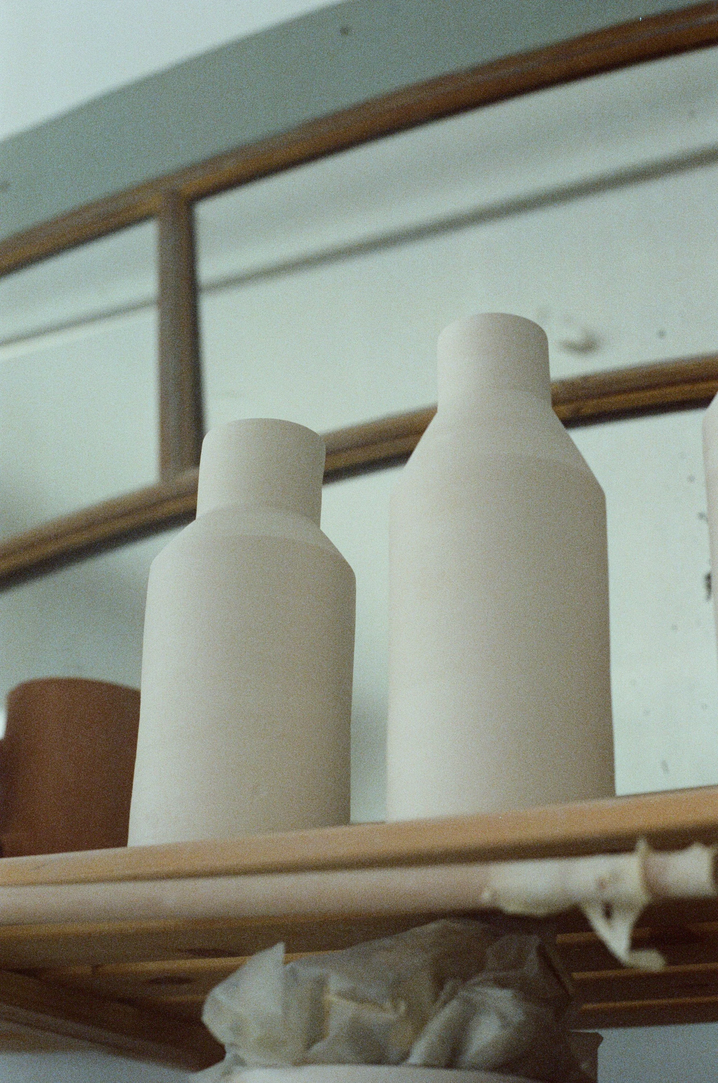 Deux bouteilles en biscuit céramique sur une étagère en bois, avec un miroir en arrière-plan.