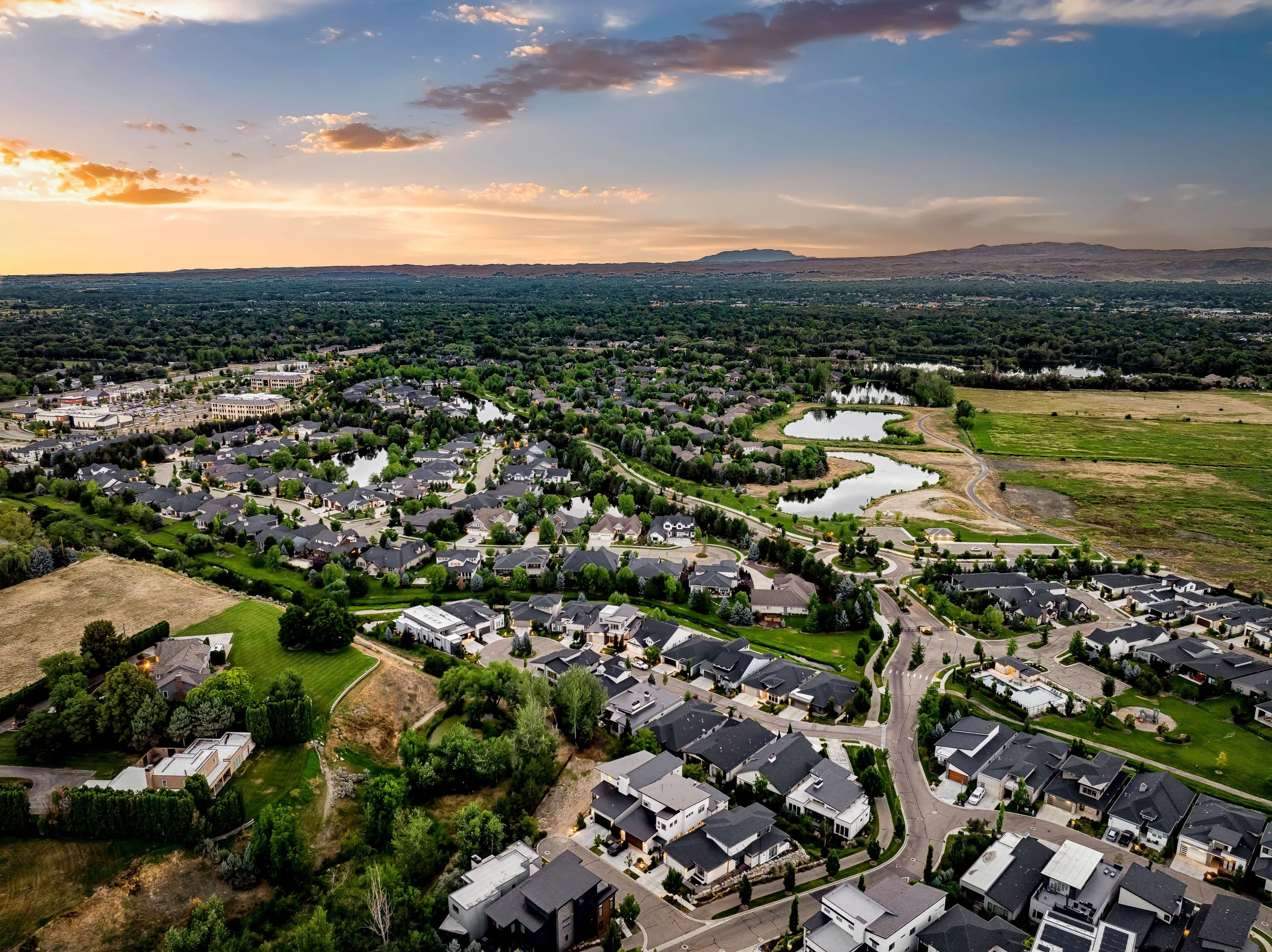 Aerial view of the Lakemoor neighborhood in Eagle, Idaho at sunset, with lakes, luxury homes, and foothills in the distance