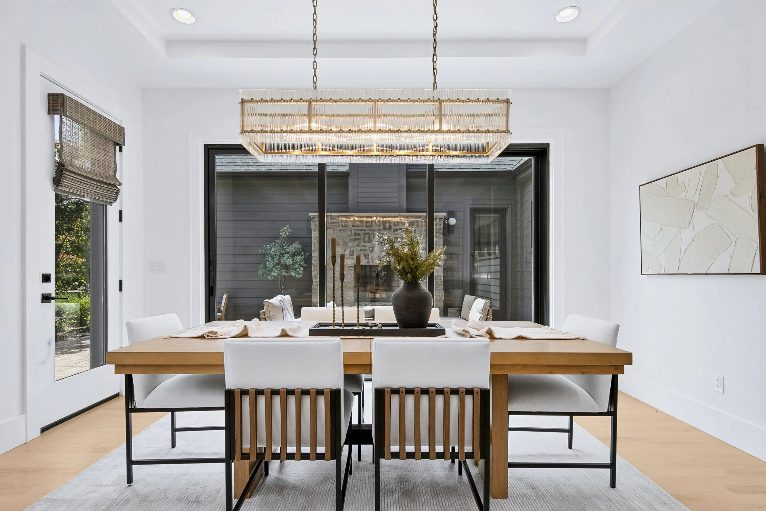  Staged luxury dining room with statement chandelier, wood dining table, and indoor-outdoor fireplace views 