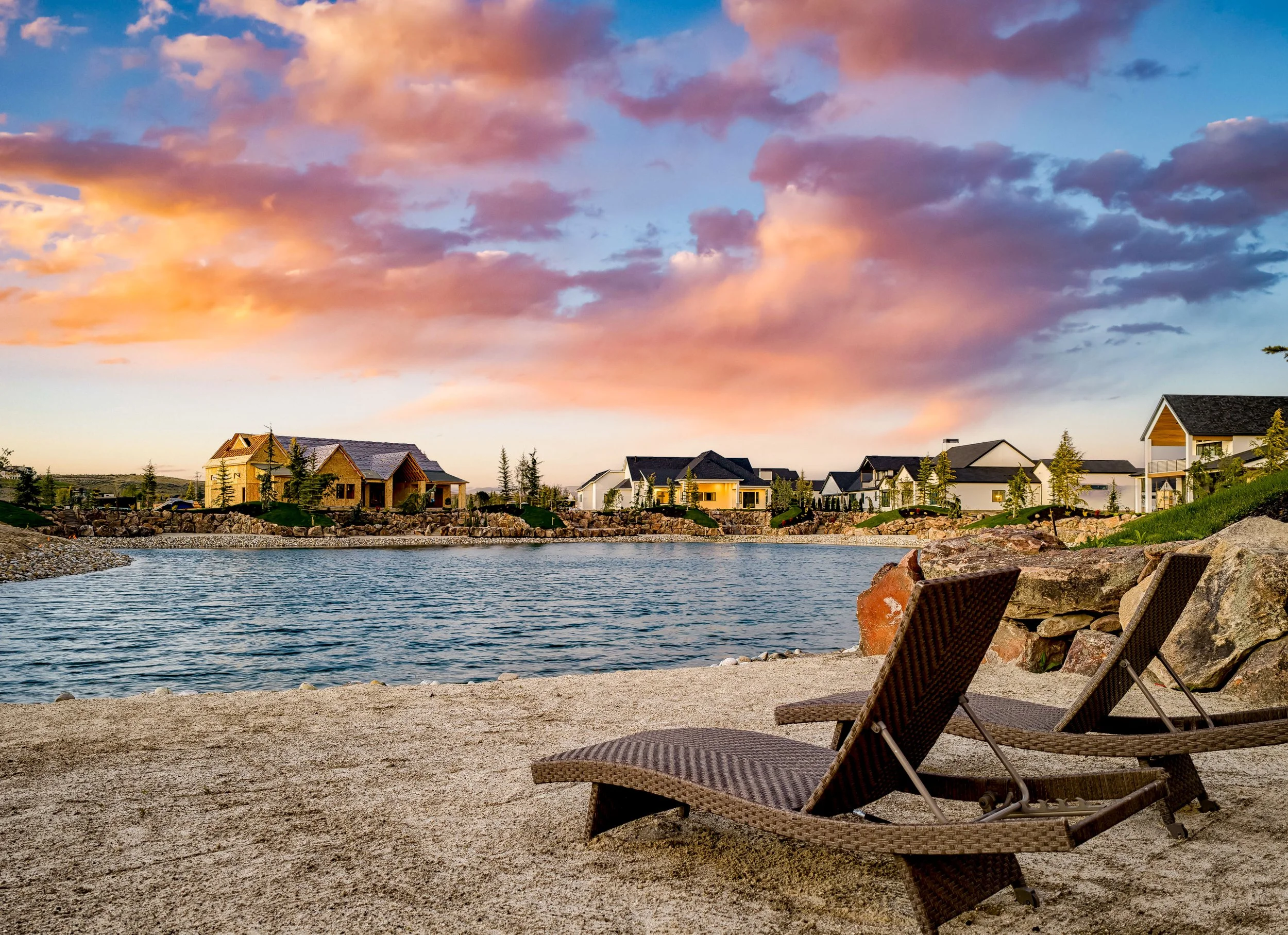 Sunset over a private lake beach at Terra View in Eagle, Idaho, with lounge chairs on the sand and custom homes across the water