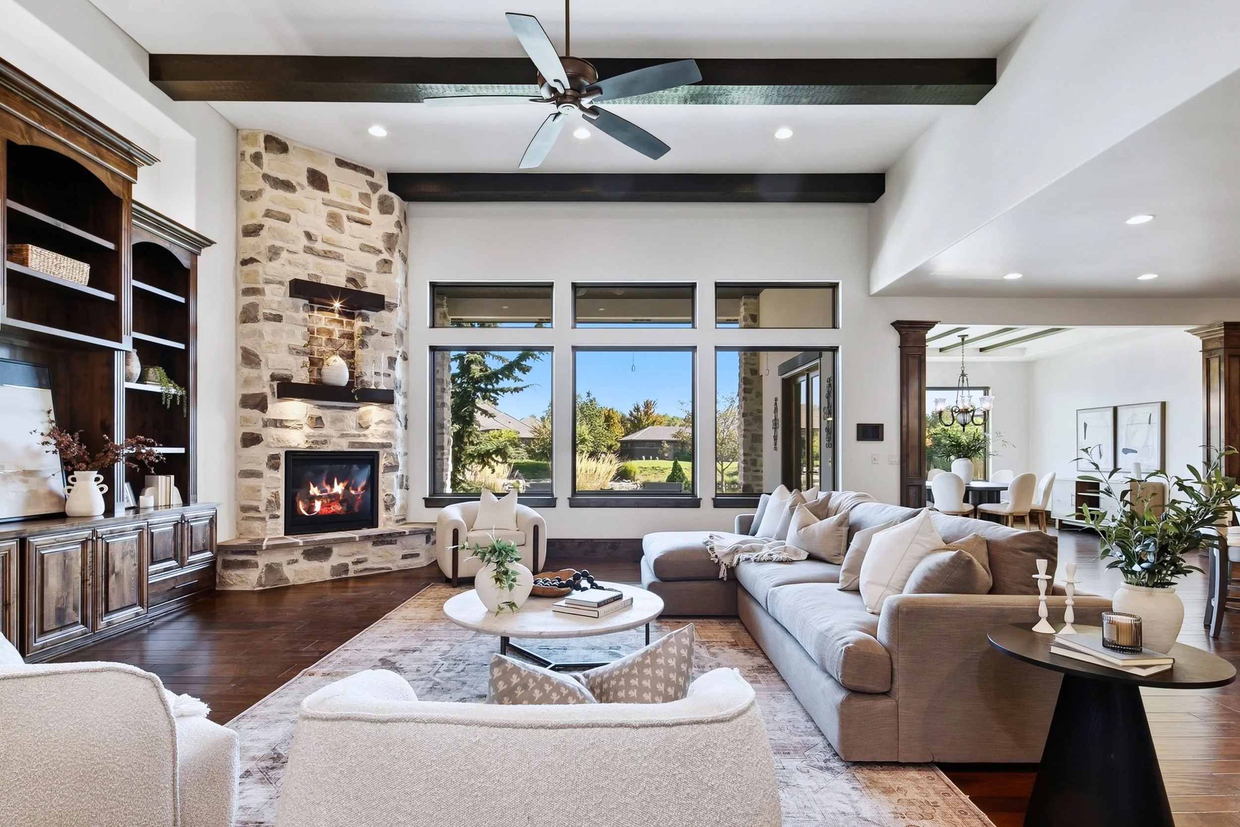 Staged great room with built in shelving and floor to ceiling fireplace, view of dining room in the background, in a luxury home in The Shores