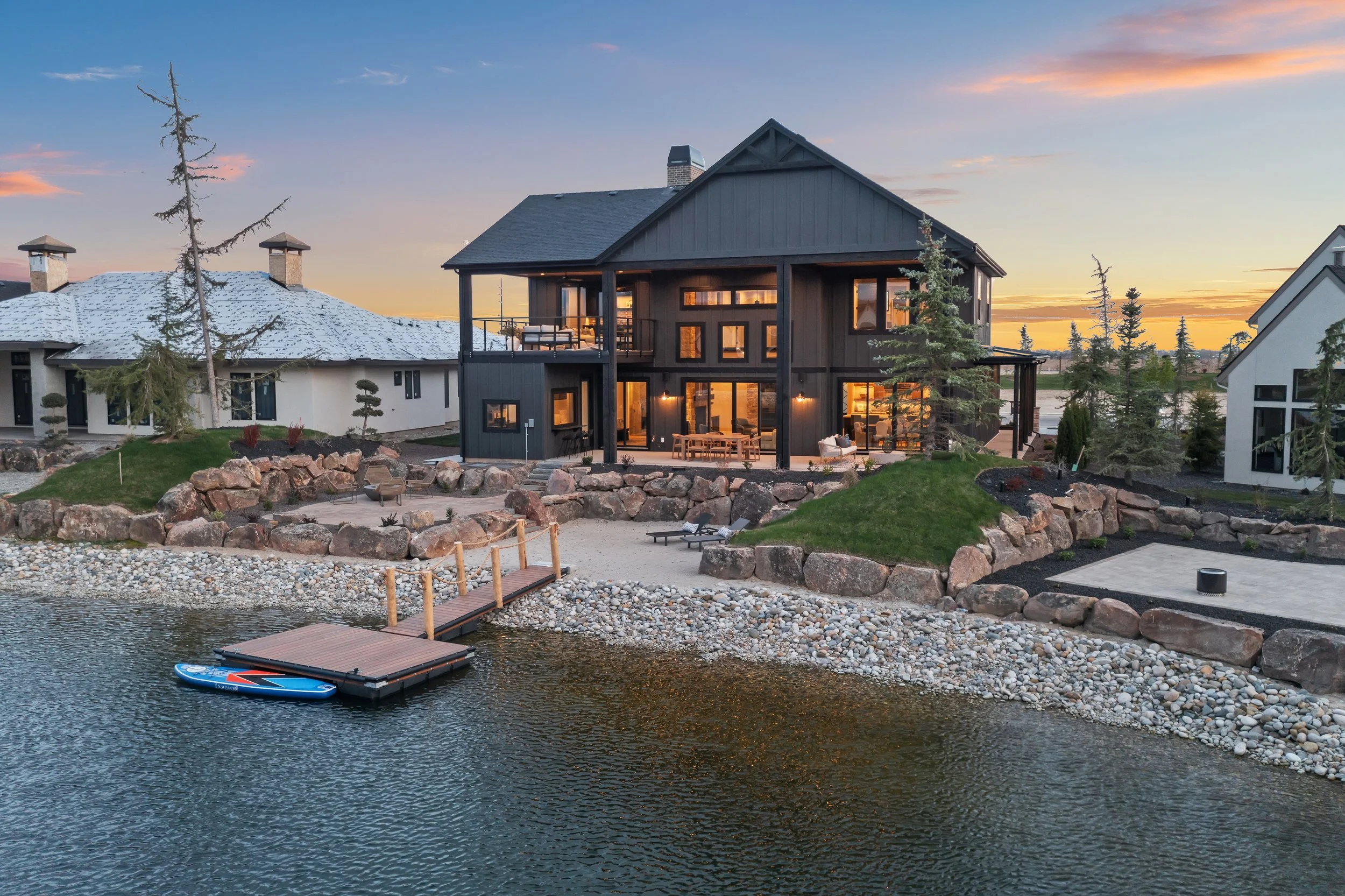 Custom home at dusk with a private dock, terraced rock landscaping, and dark siding on the exterior