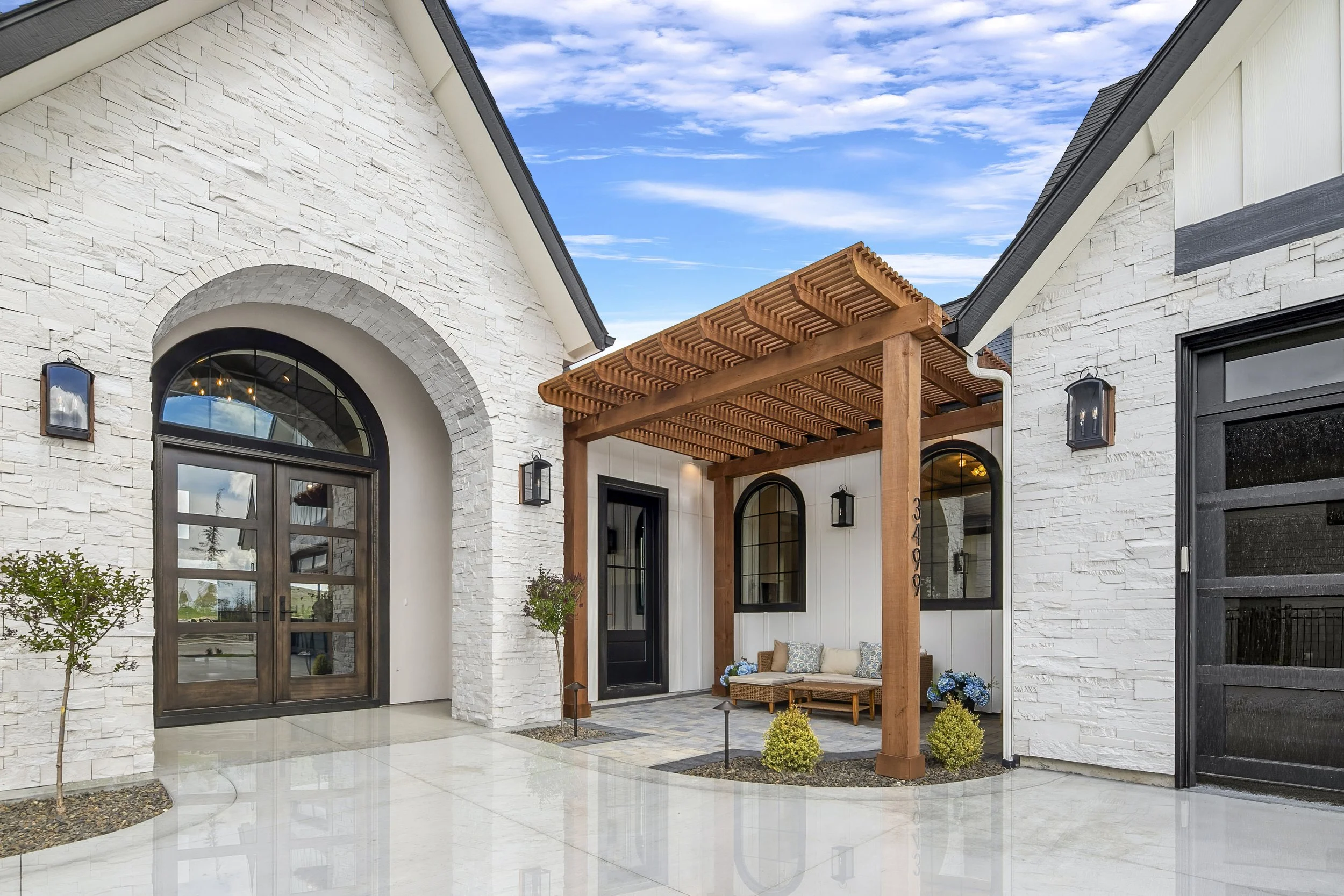 Luxury home exterior with white stone facade, arched entryway, and a covered wood pergola patio