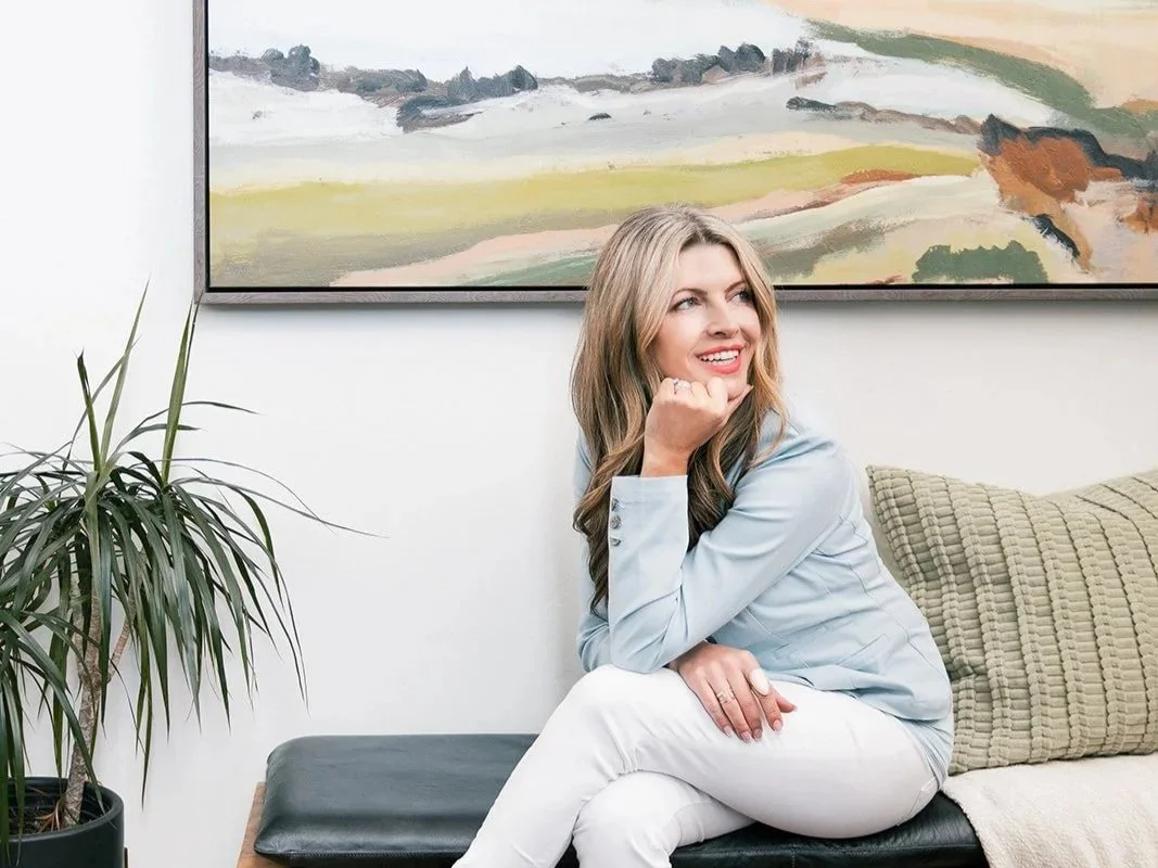 Rachel Postigo, luxury Realtor in Eagle, Idaho, seated and smiling in a bright, art-filled room