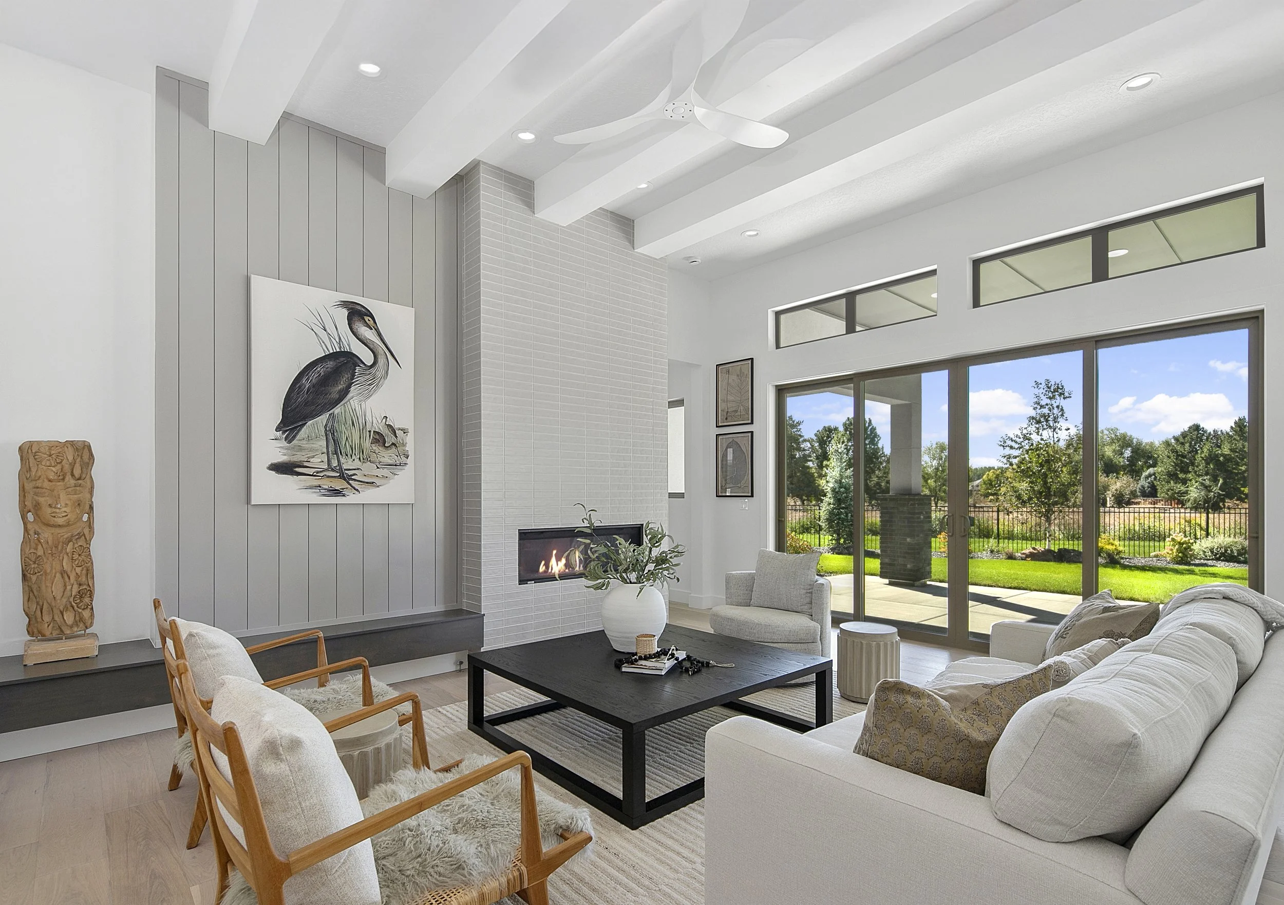 Bright luxury living room with a vaulted beamed ceiling, fireplace, and sliding glass doors to the backyard