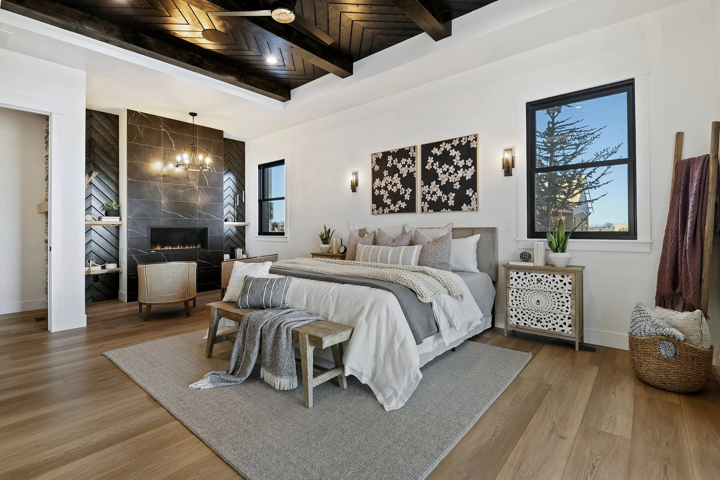 Luxury primary bedroom with black marble fireplace, herringbone wood-beam ceiling, and large windows in an Eagle, Idaho home