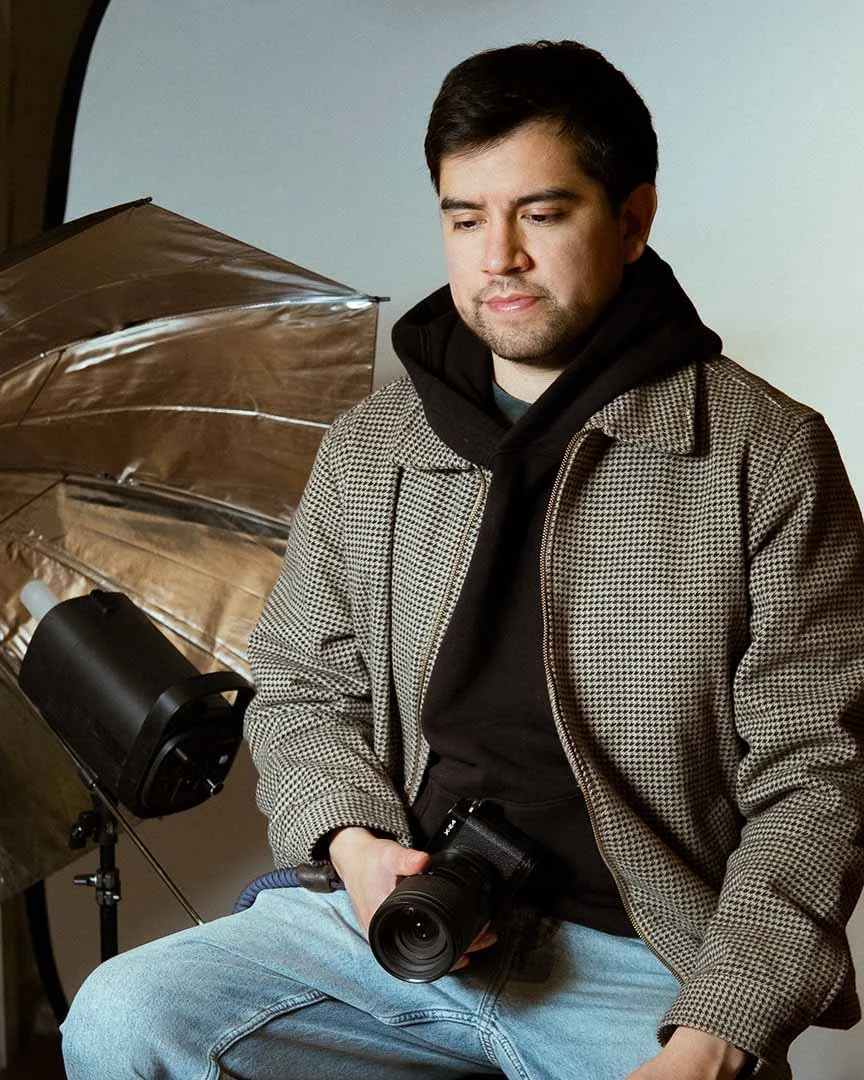 A photographer sitting in his headshot studio in a vintage jacket with dramatic lighting