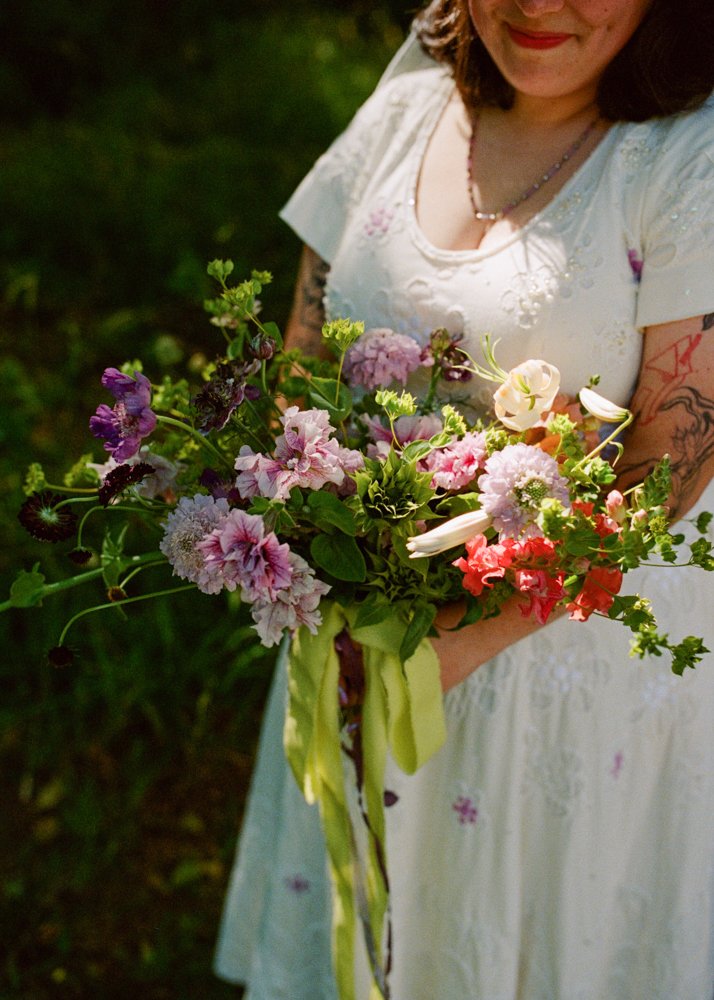A close-up of a woman holding a beautiful wedding bouquet of greens, pinks, whites, and reds. Photographed by Seattle wedding photographer Holly Stevens.