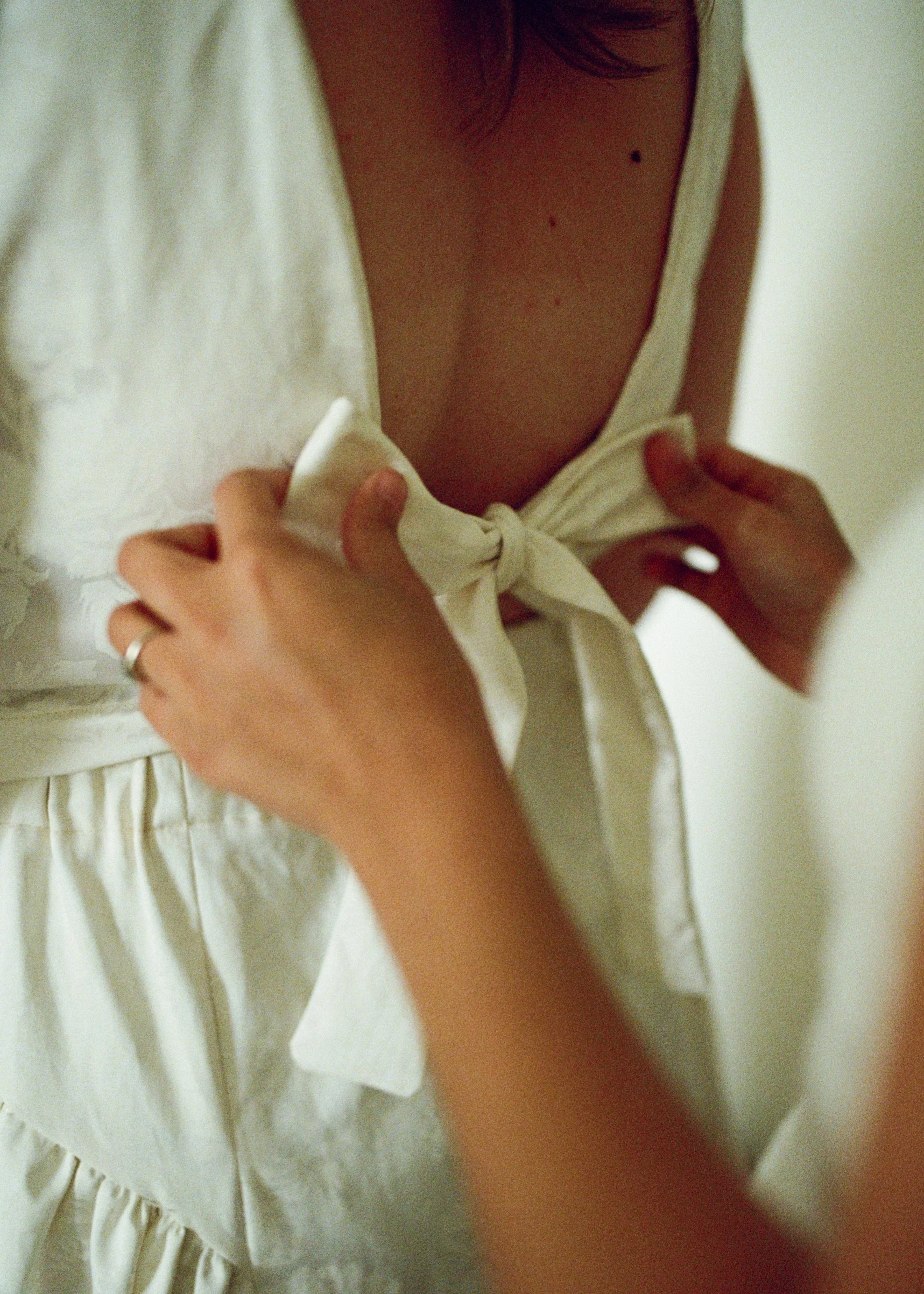 A close-up shot of a woman’s hands tying the bow on her bride’s wedding dress. Photographed by queer wedding photographer Holly Stevens.