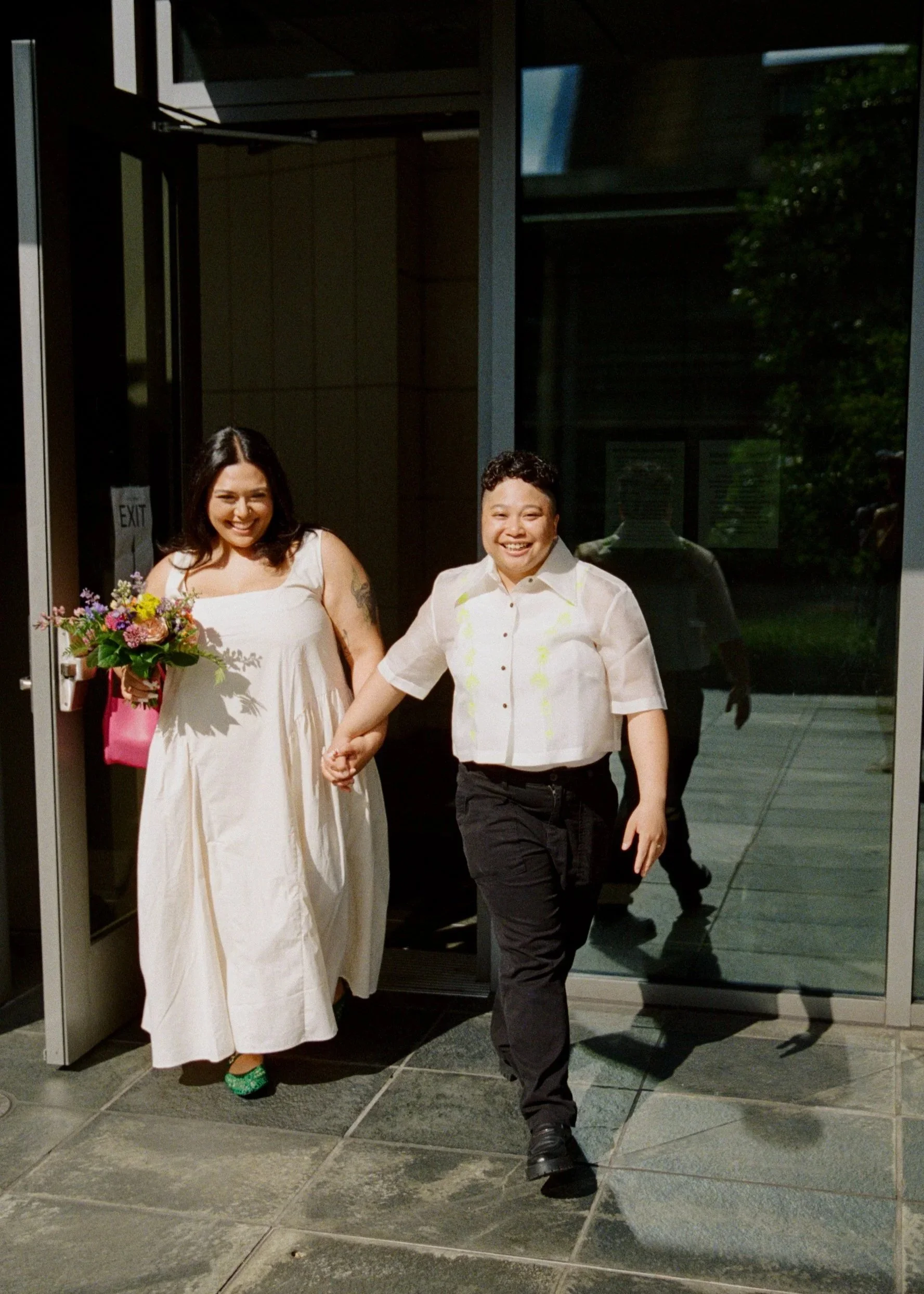 Two newly married people emerge from the Seattle Municipal Courthouse, beaming with joy. Photographed by elopement photographer Holly Stevens.