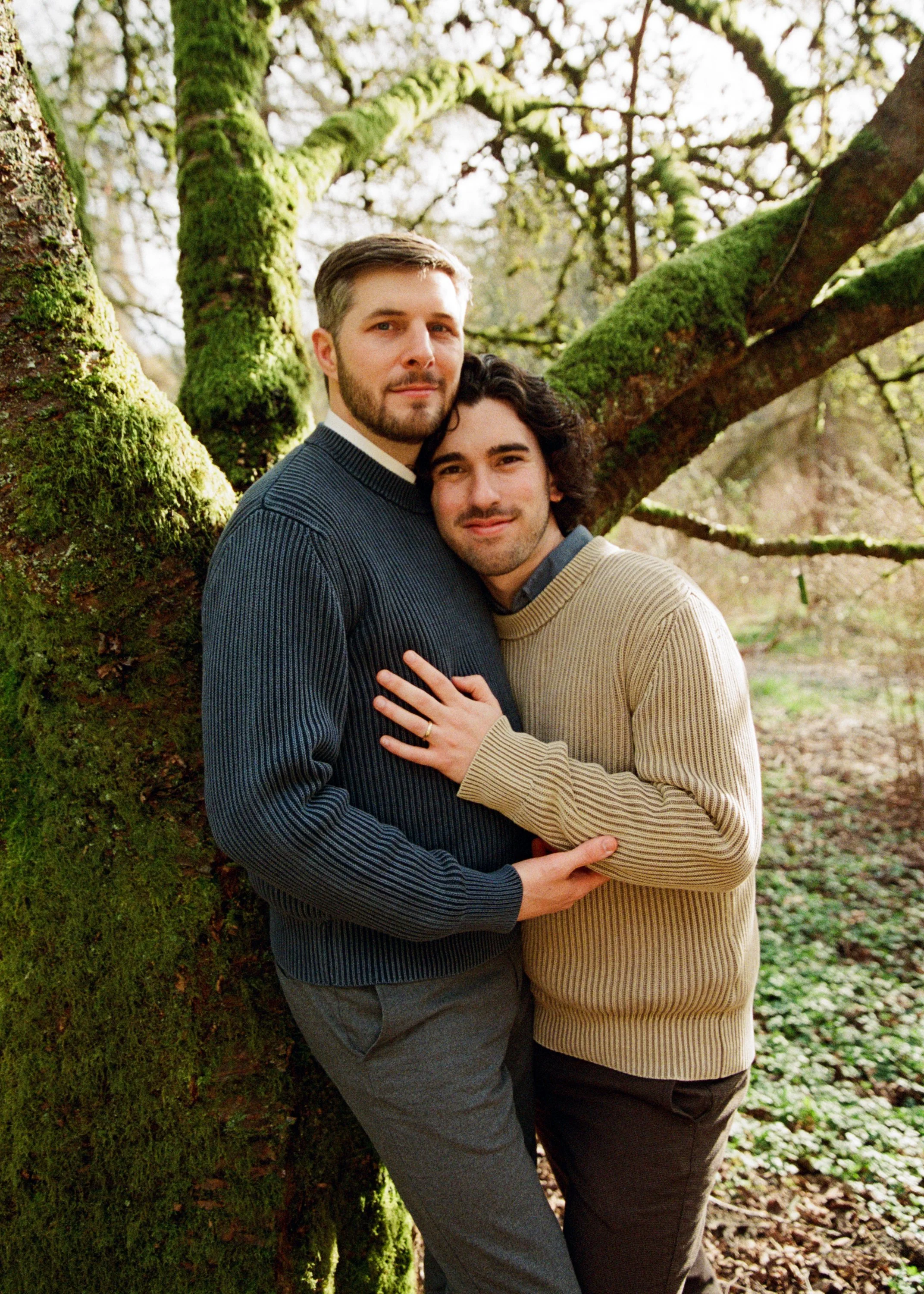 A newly married gay couple lean together in front of a tree in the Washington Park Arboretum. Photographed by LGBTQ wedding photographer Holly Stevens.