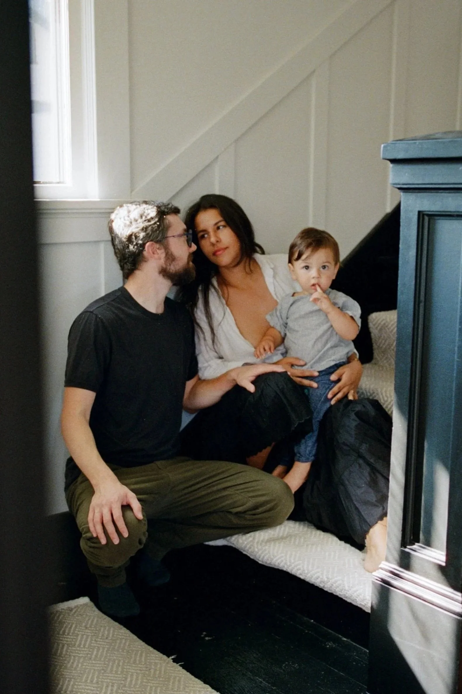 A family sits on stairs in beautiful afternoon sunlight. The two adults gaze into each other's eyes while the young child stares straight into the camera. Shot by Seattle photographer Holly Stevens.