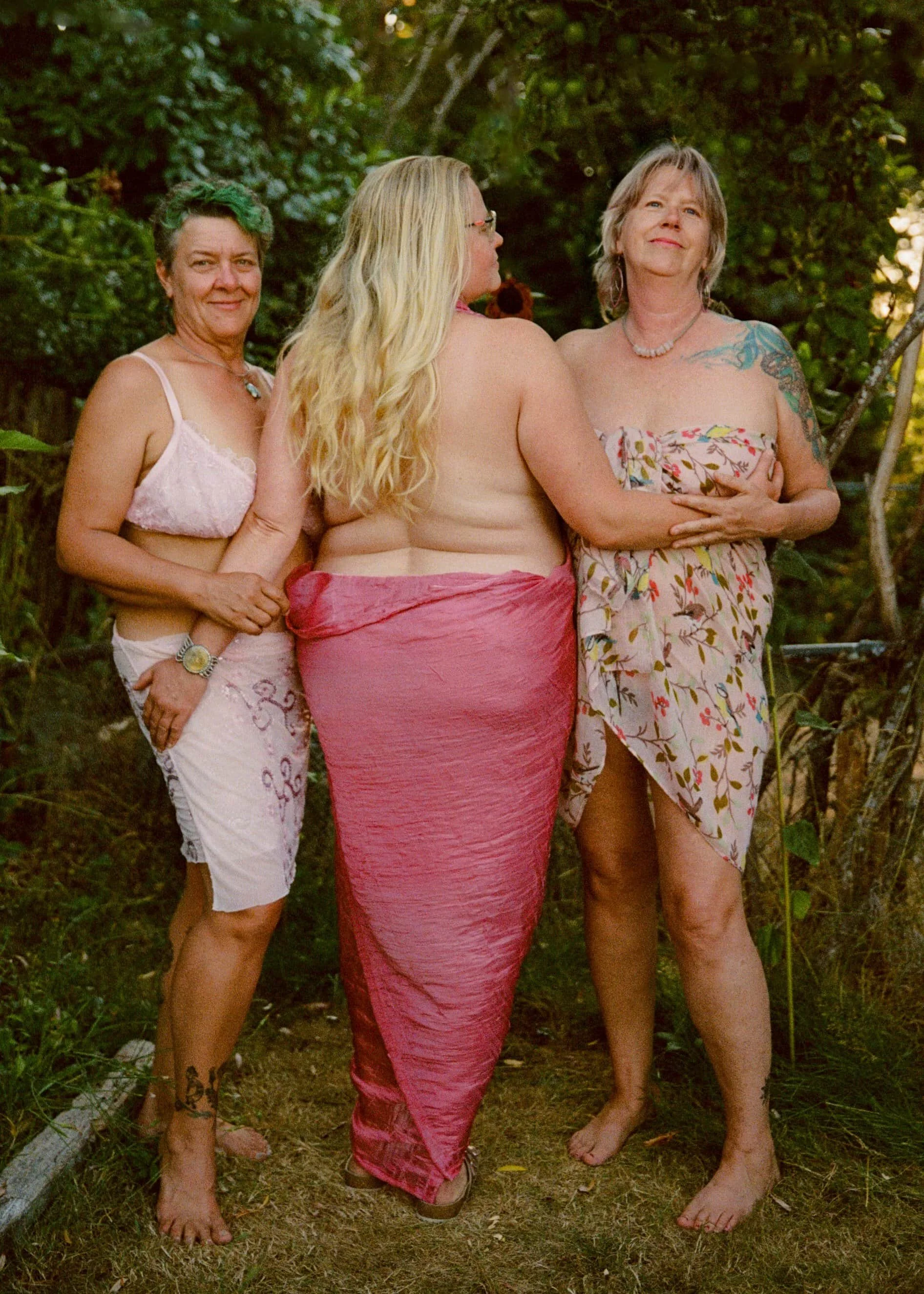 Three polyamorous women standing together embracing, two of them looking out into the sky and one looking back.
