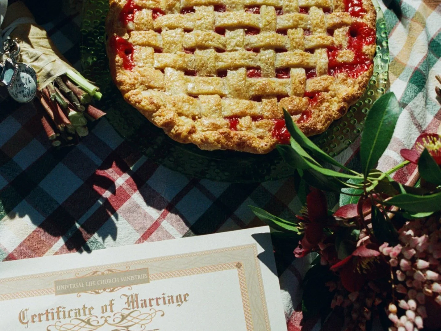 A close-up of a delectable cherry pie sitting on a gingham tablecloth alongside a wedding certificate. Photographed by PNW wedding photographer Holly Stevens.