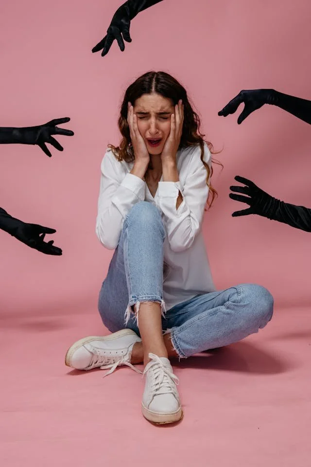 A woman covering her face with 5 dark hands reaching toward her head