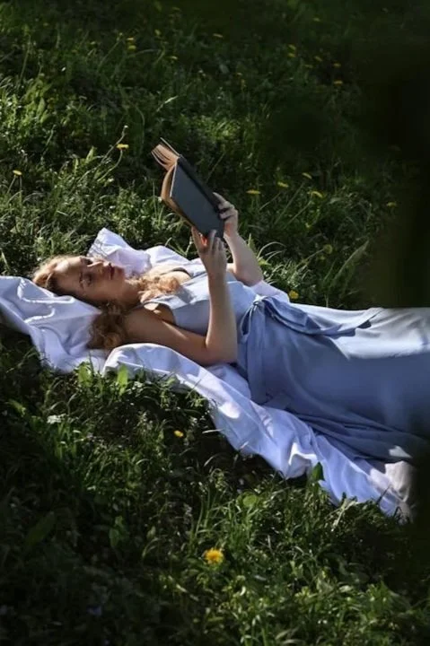 A woman laying on a blanket in the grass reading a book