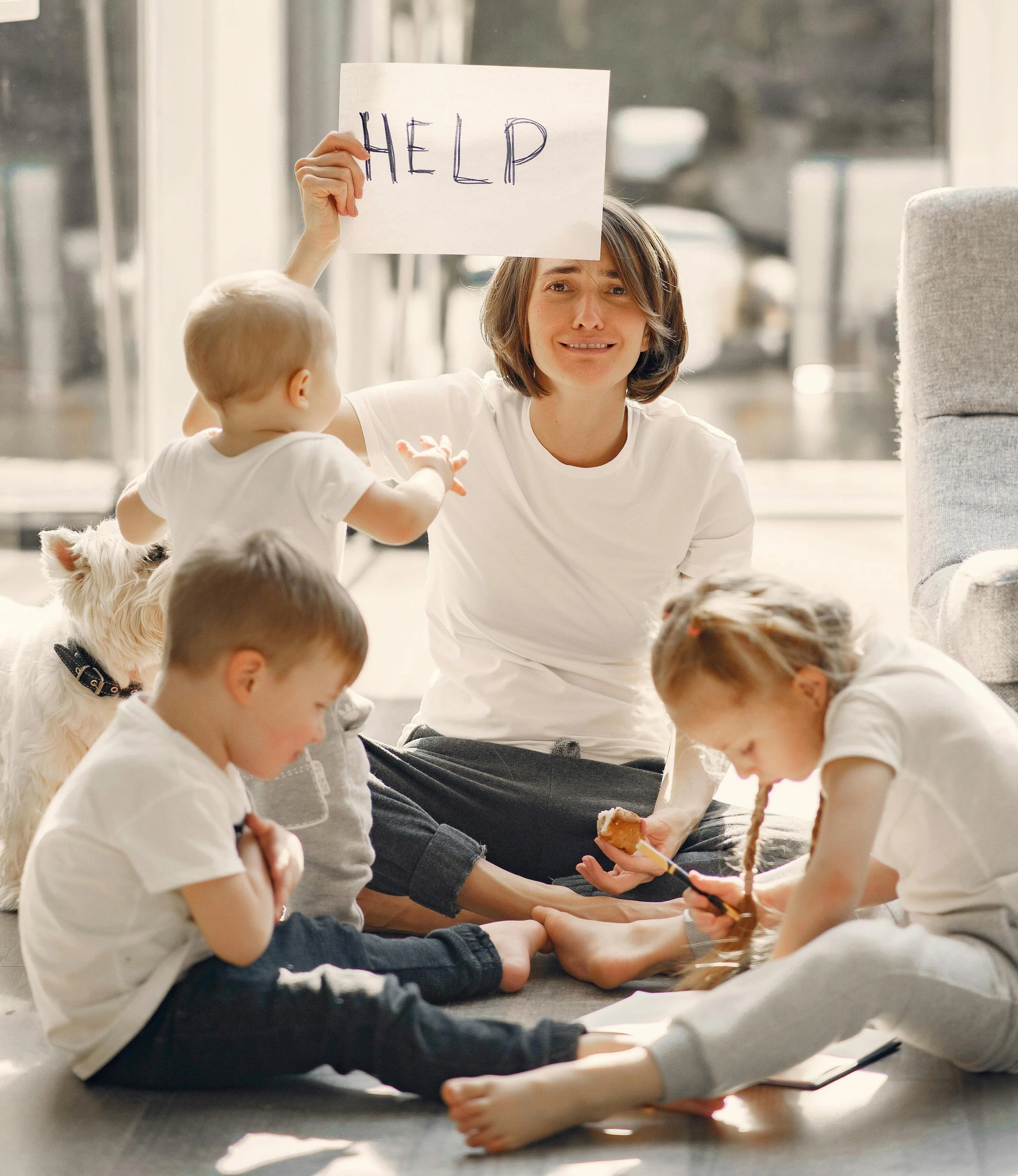 A mother holding a sign that says "help" as she plays with her children