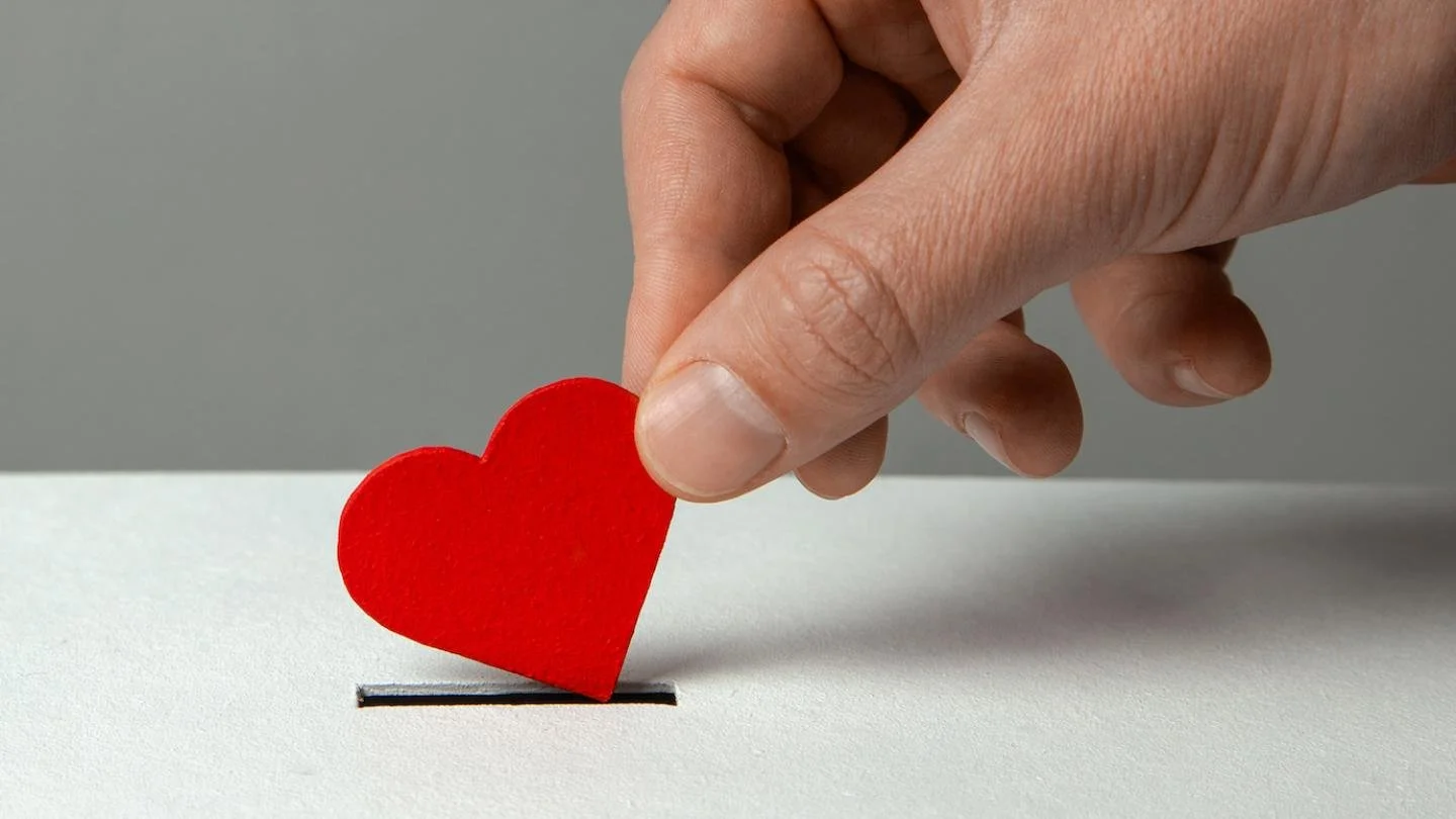 A hand placing a red paper heart into a ballot box for voting