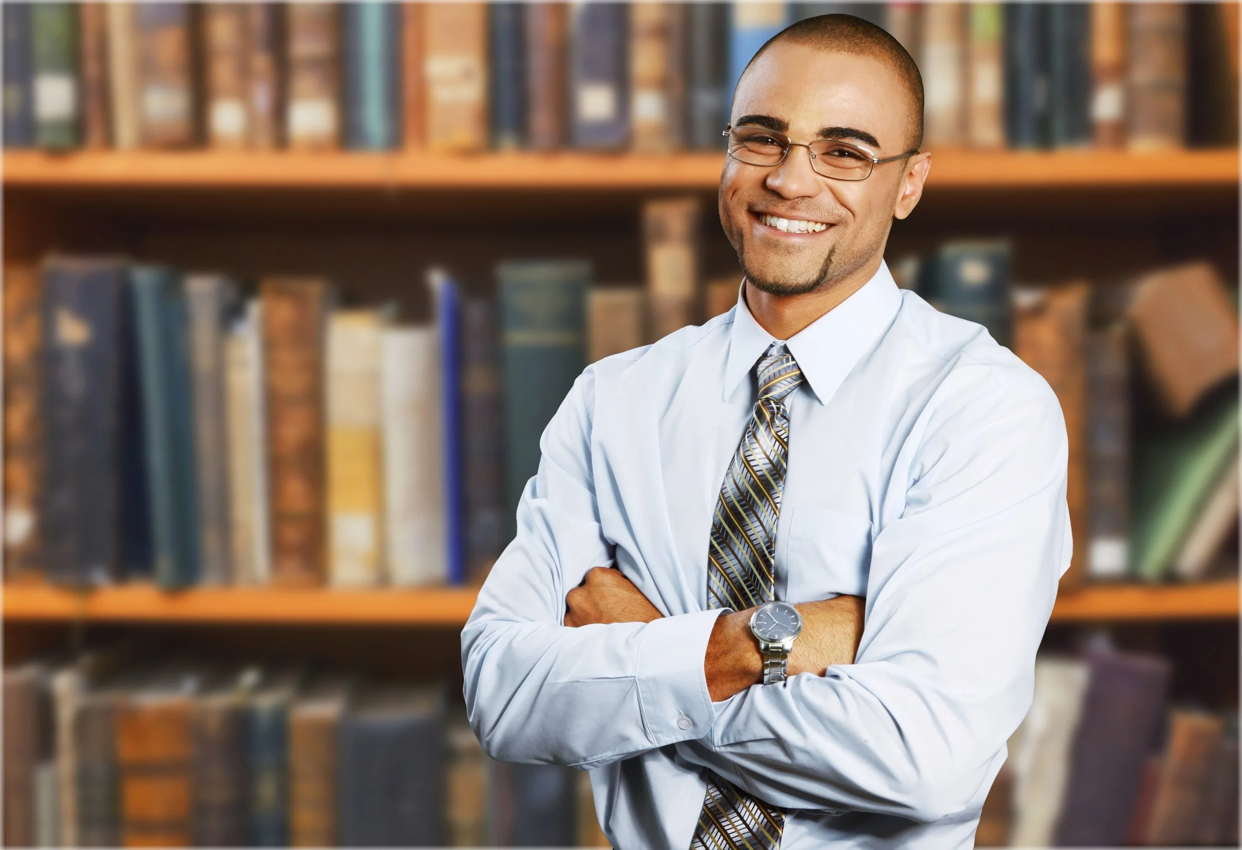 Man in shirt and tie crosses arms and faces camera while smiling