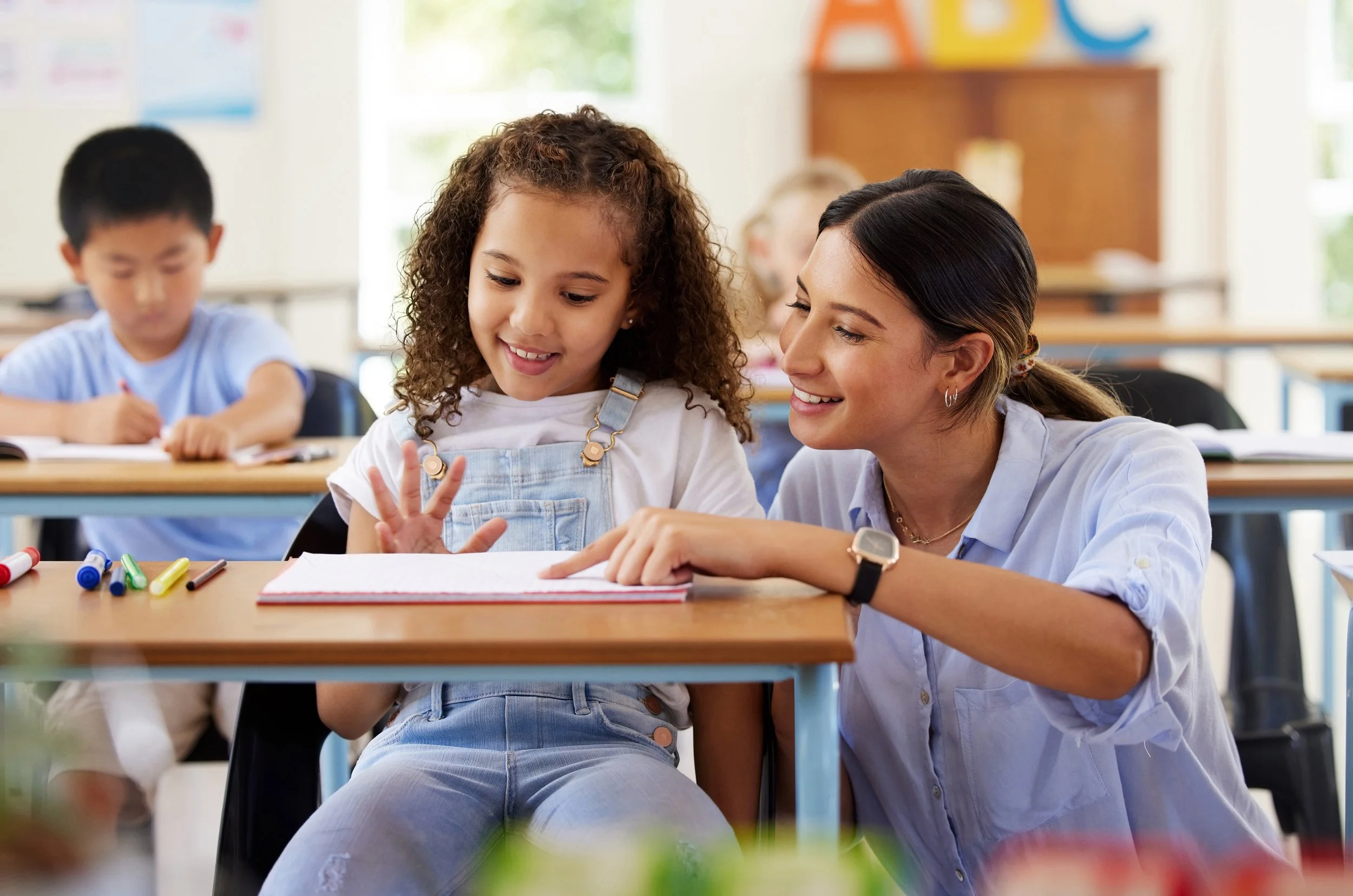 Teacher is reading with young girl at a desk
