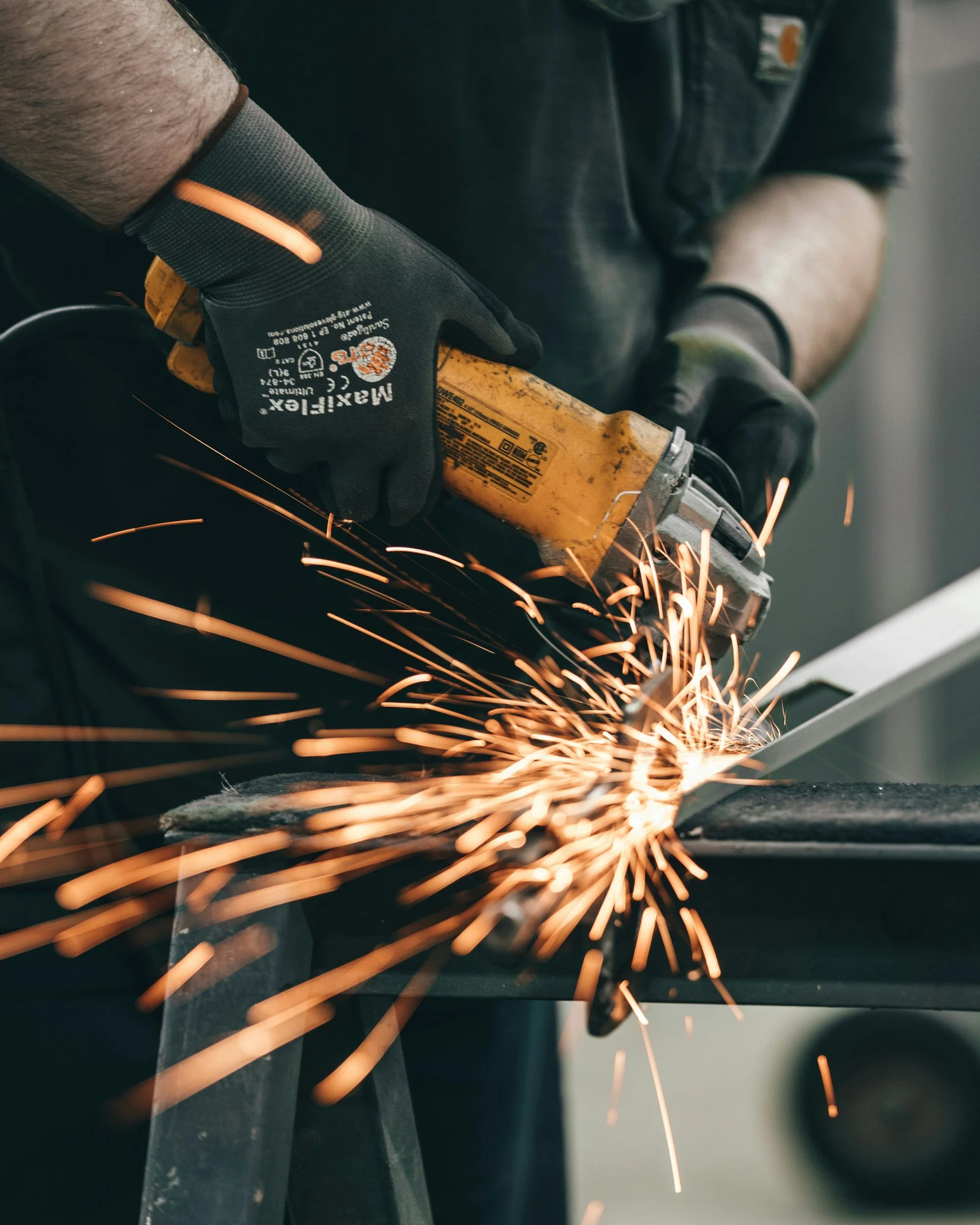 Person using an angle grinder, producing sparks, while wearing gloves in a workshop.
