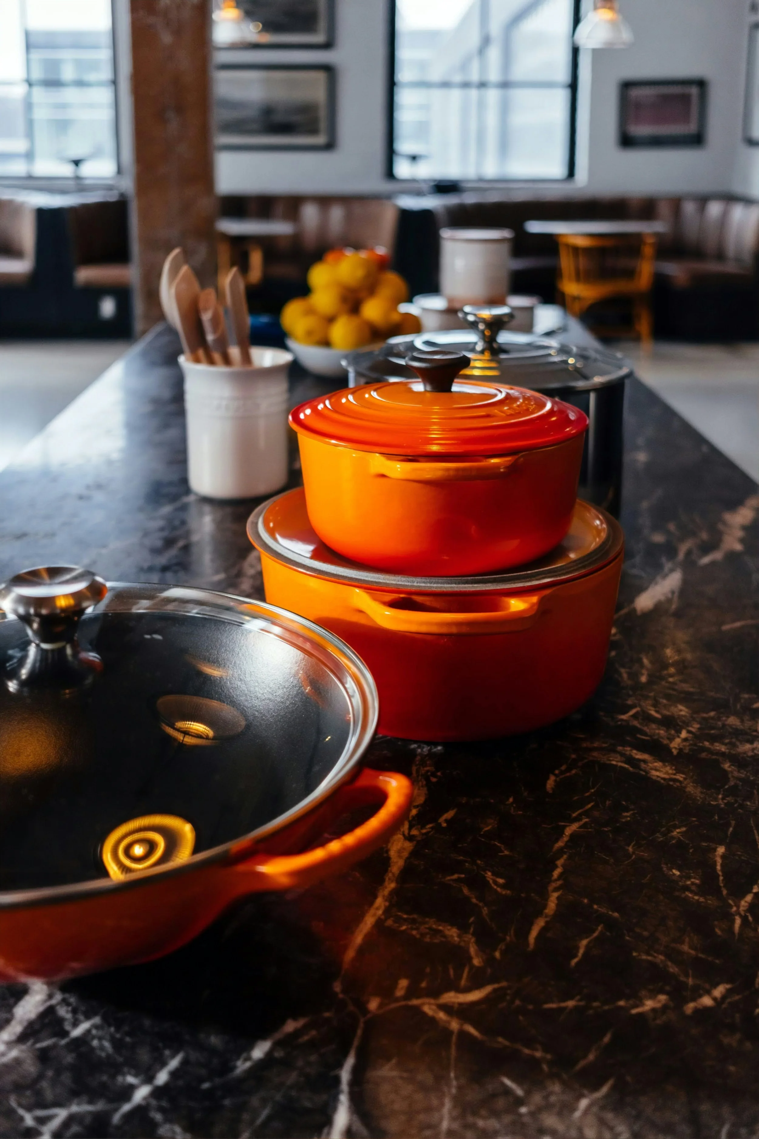 Orange cookware set on a black marble countertop with lemons in the background in a modern kitchen setting.