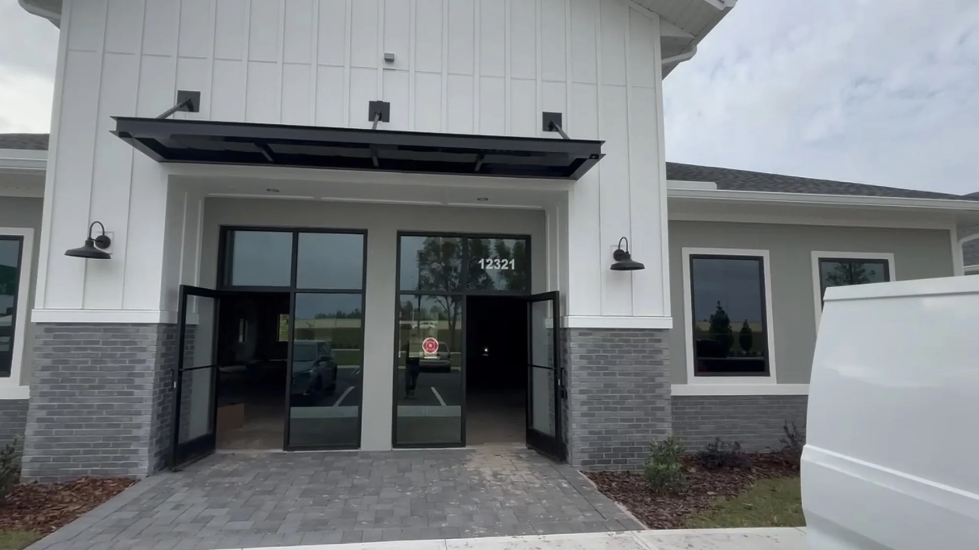 Modern commercial building entrance with glass doors, brick and siding exterior, house number 12321, and exterior lamps.