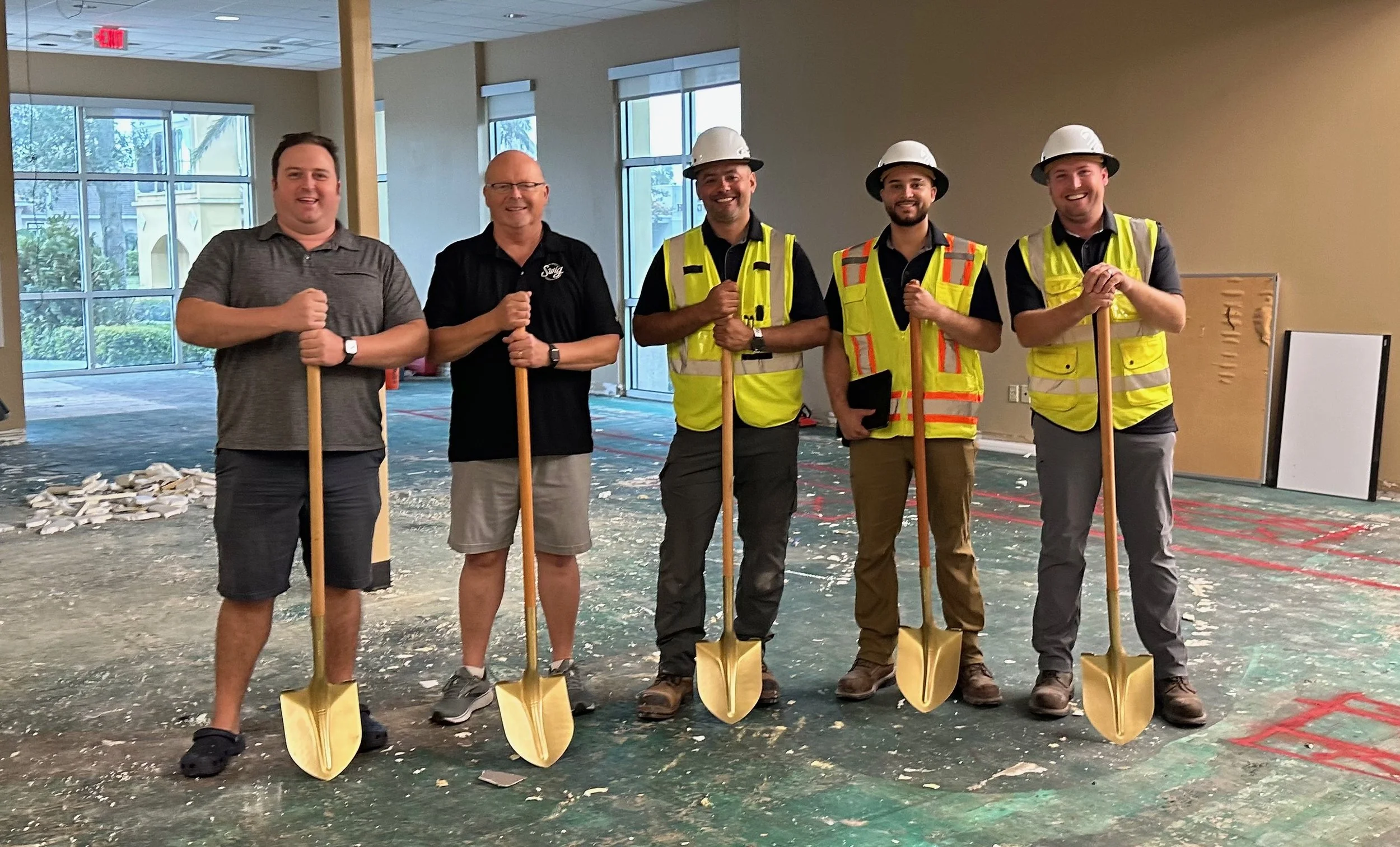 Group of five men with shovels at a construction site indoors