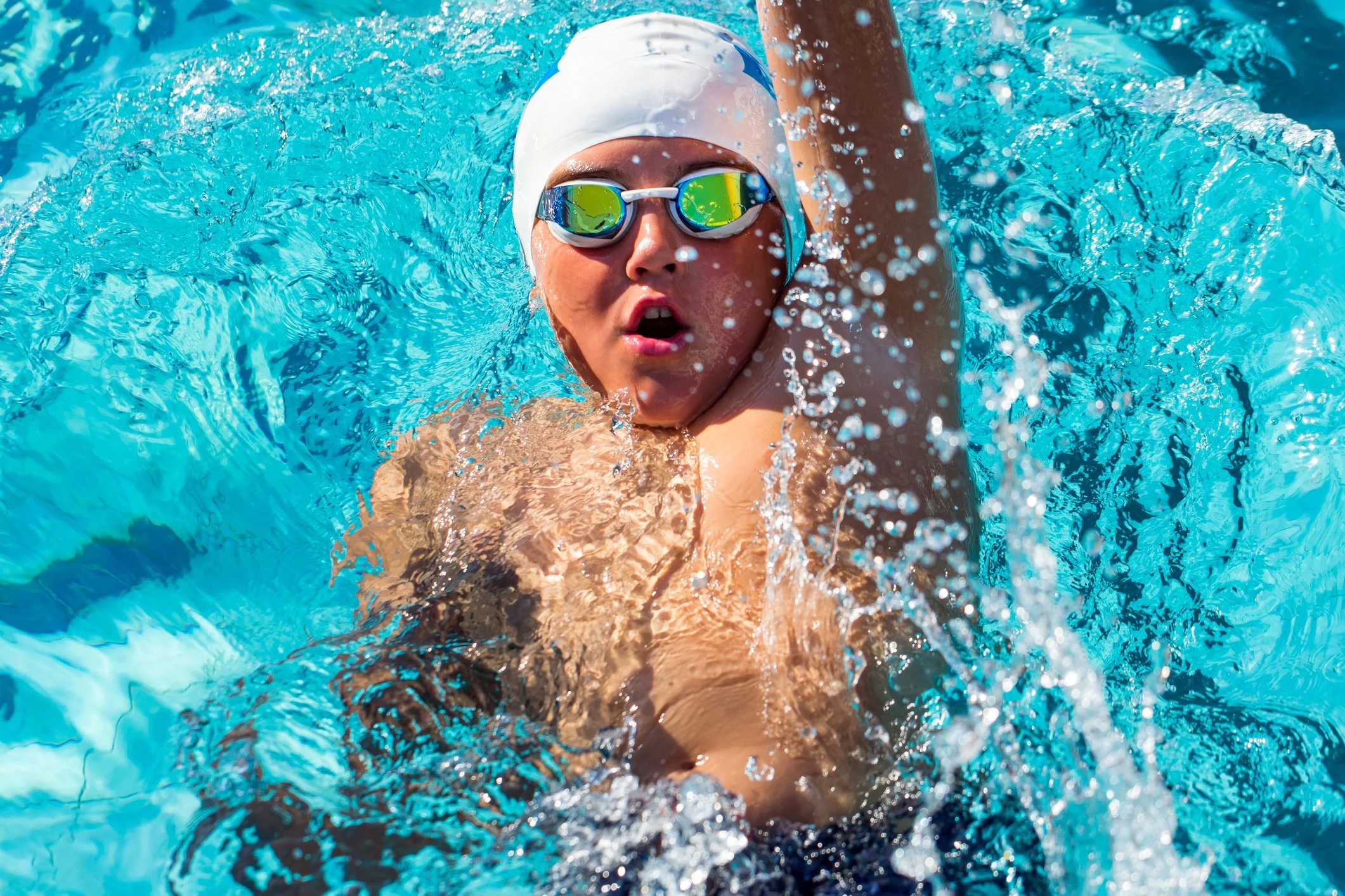 A female swimmer wearing goggles, a white swim cap, and a swimsuit swimming in a pool.
