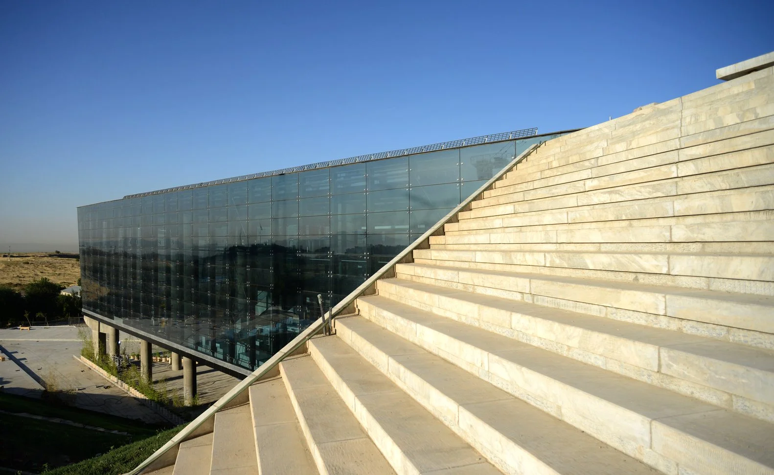 Modern glass building next to wide stone steps under a clear blue sky.