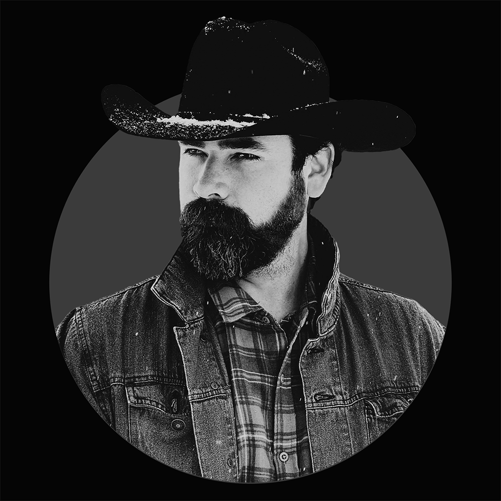 Black and white portrait of a man wearing a cowboy hat, denim jacket, and checkered shirt, with a beard and mustache, looking off to the side.
