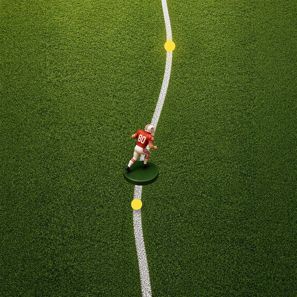A miniature figurine of an American football player on a football field with yard lines, positioned on the white line near the center.