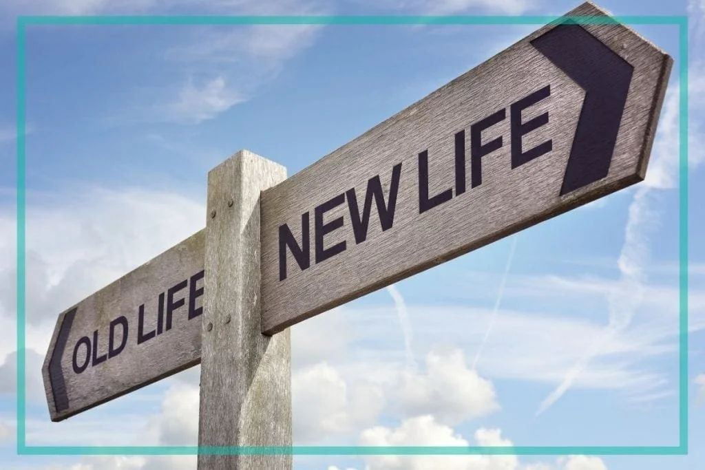 Directional signpost with arrows labeled "Old Life" pointing left and "New Life" pointing right against a blue sky with clouds.