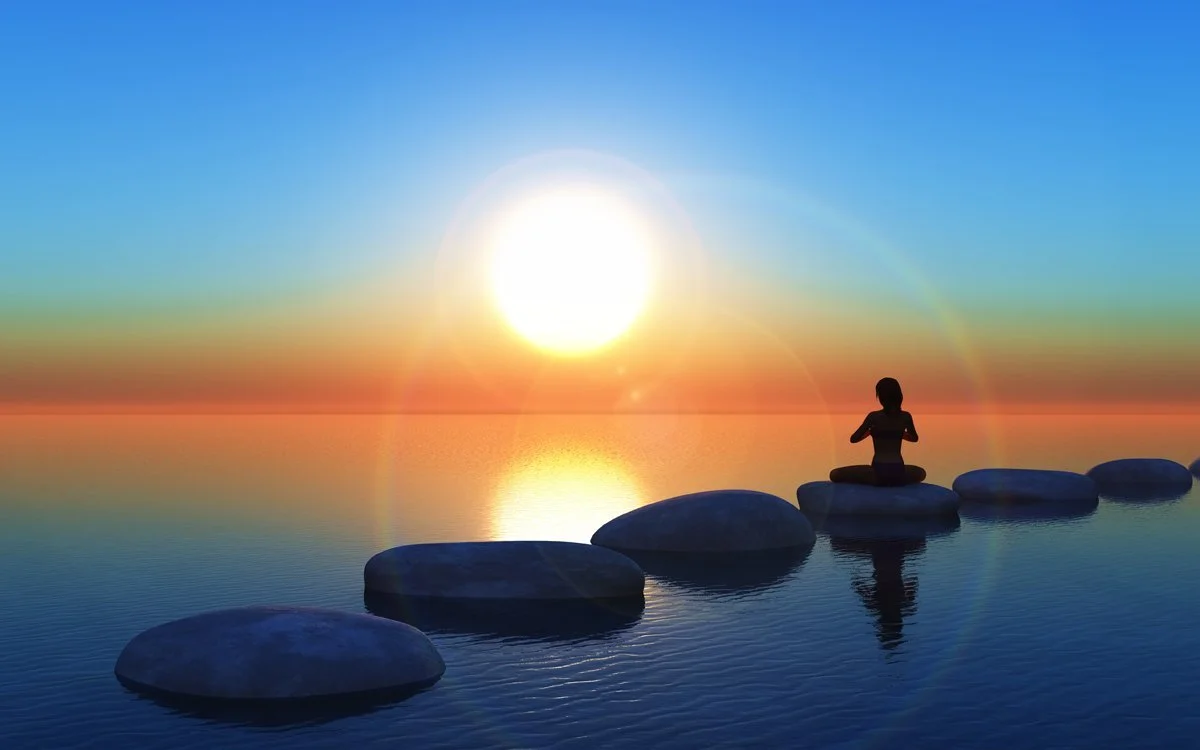 Person meditating on stepping stones in water during sunset.