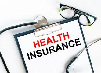 Clipboard with "Health Insurance" in red and black text, stethoscope, and eyeglasses on a white background.
