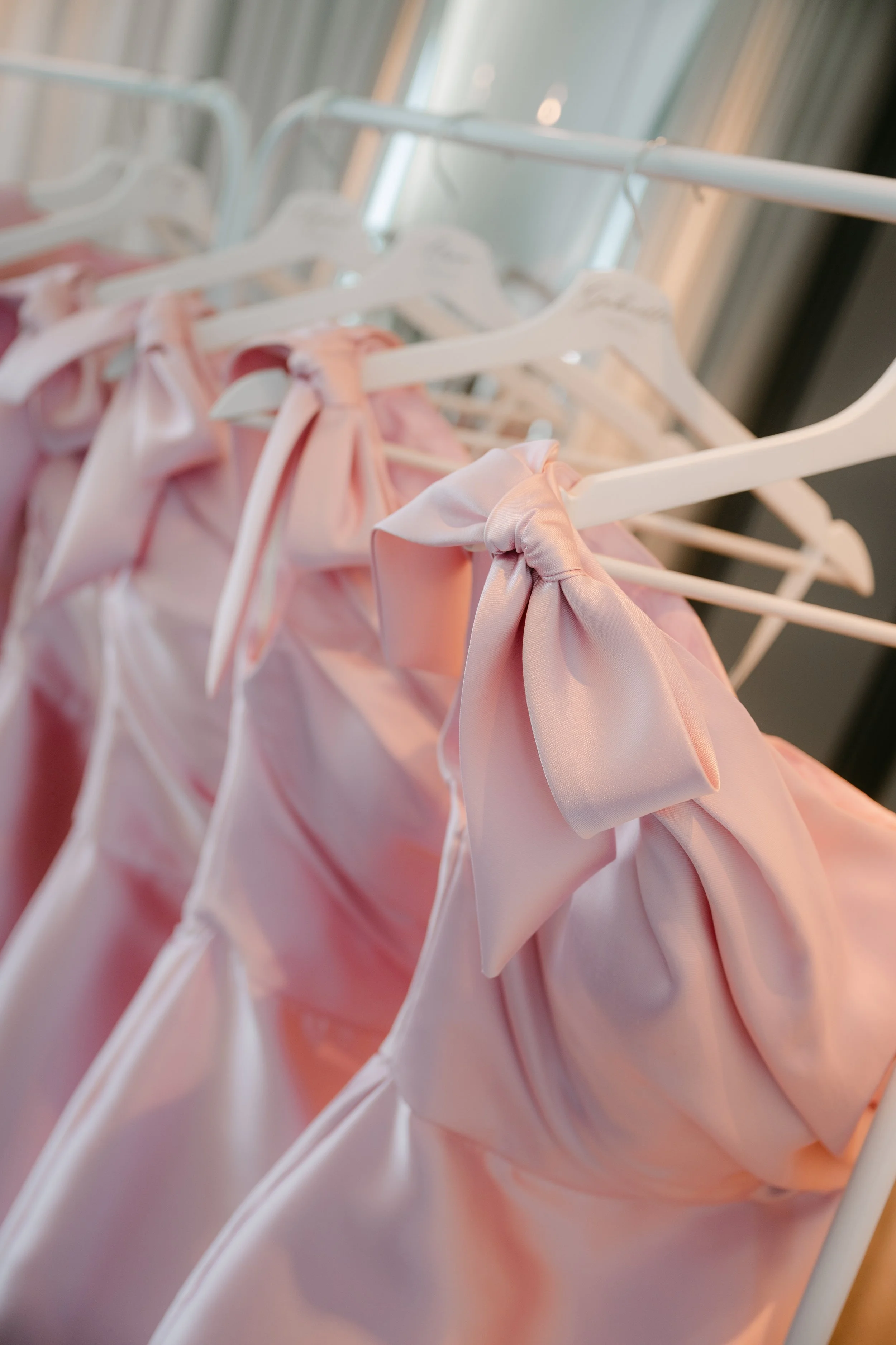 5 pink custom bridesmaid's gowns on a garment rack with bow detailing