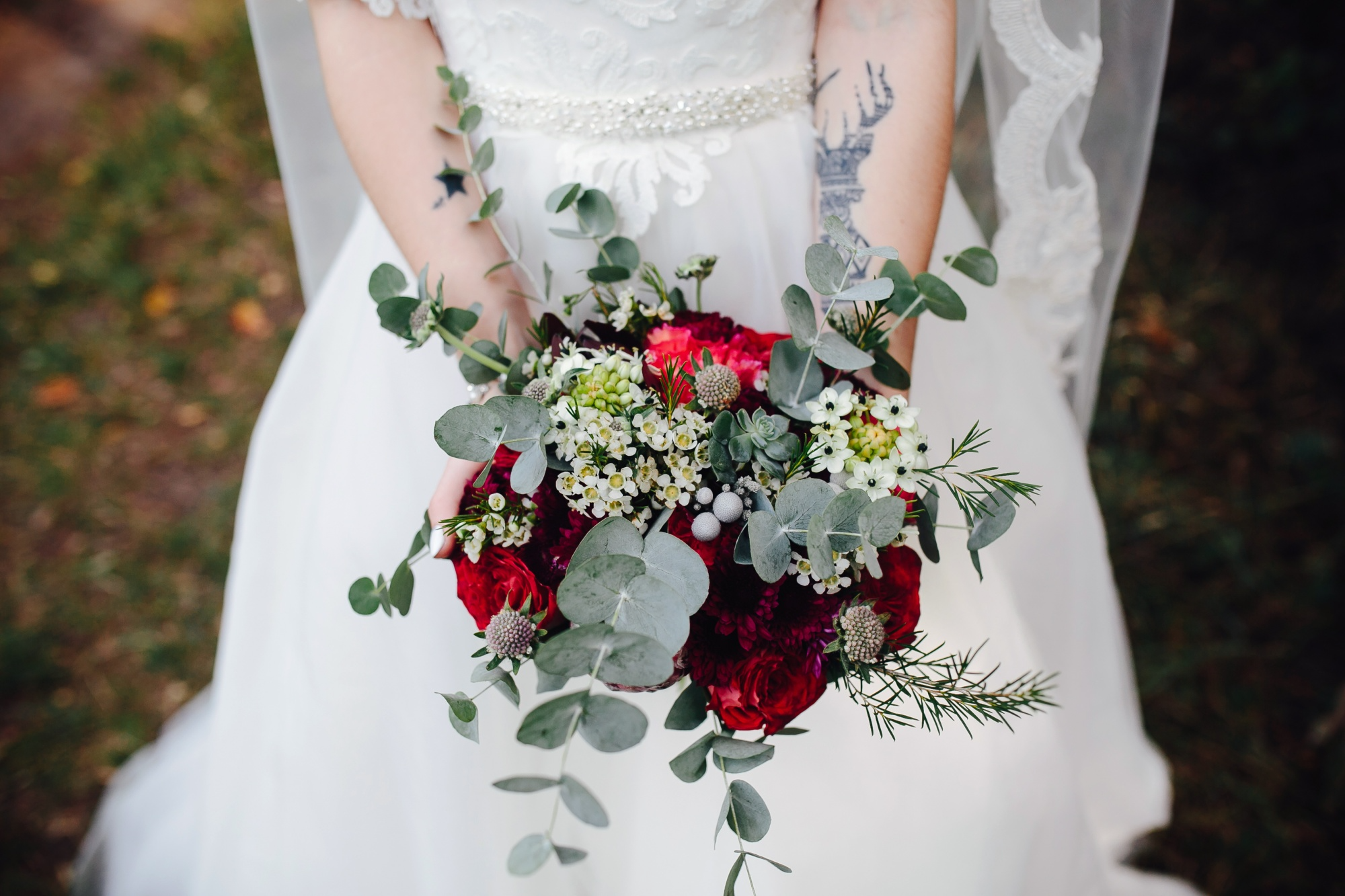 Bride holding a wedding bouquet of red roses, eucalyptus and white wax flowers for choosing wedding corsage flowers