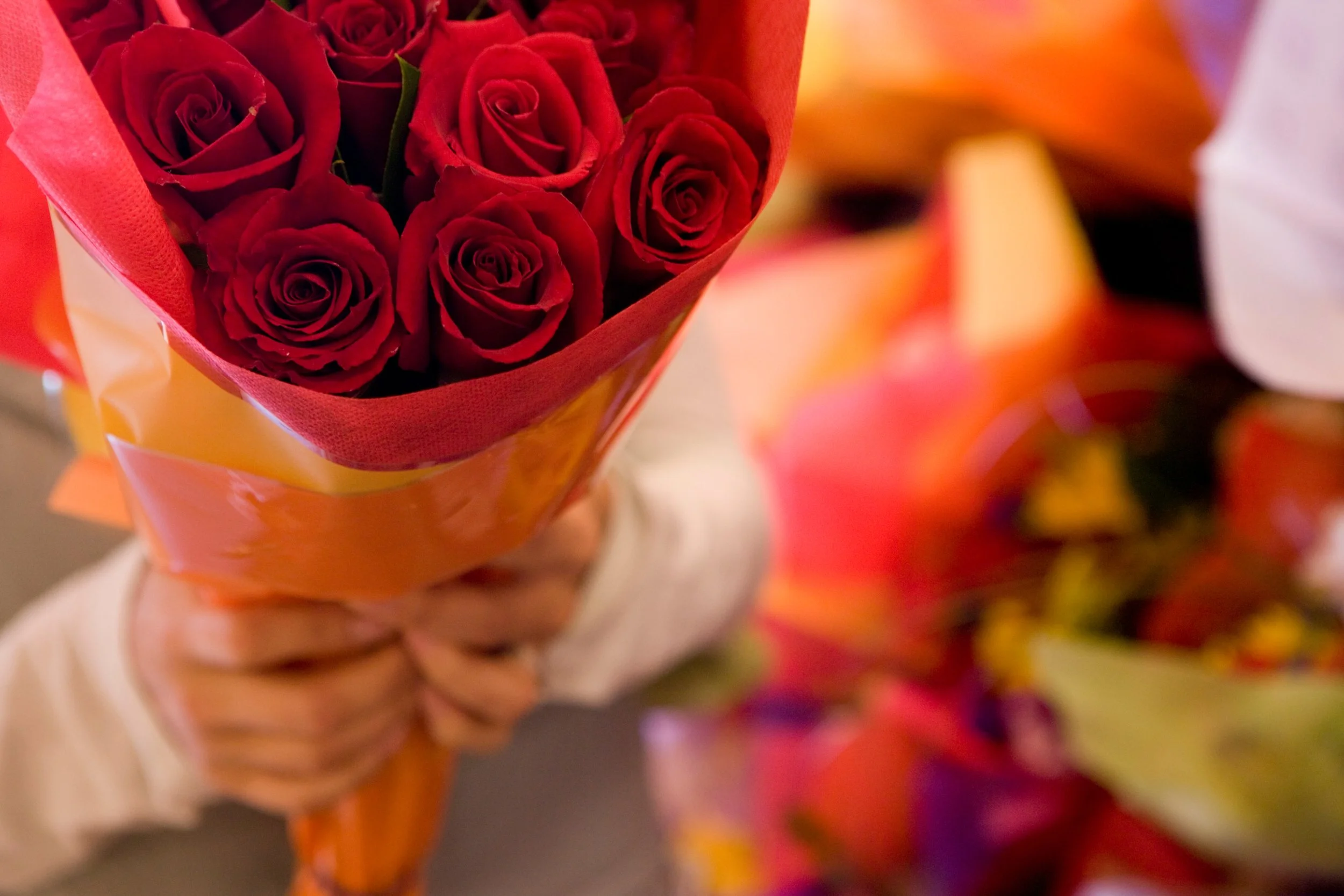 A close-up view of someone holding a vibrant arrangement of deep red roses wrapped in orange paper, a classic style for a Valentine’s Day bouquet in Singapore