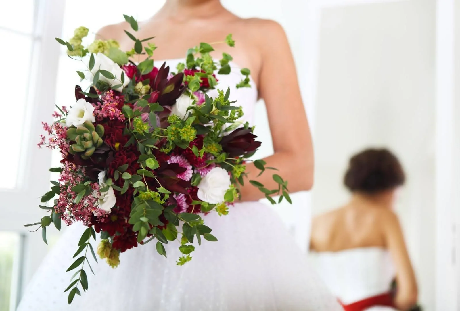 Close-up of a bride in a white dress holding a rustic wedding bouquet