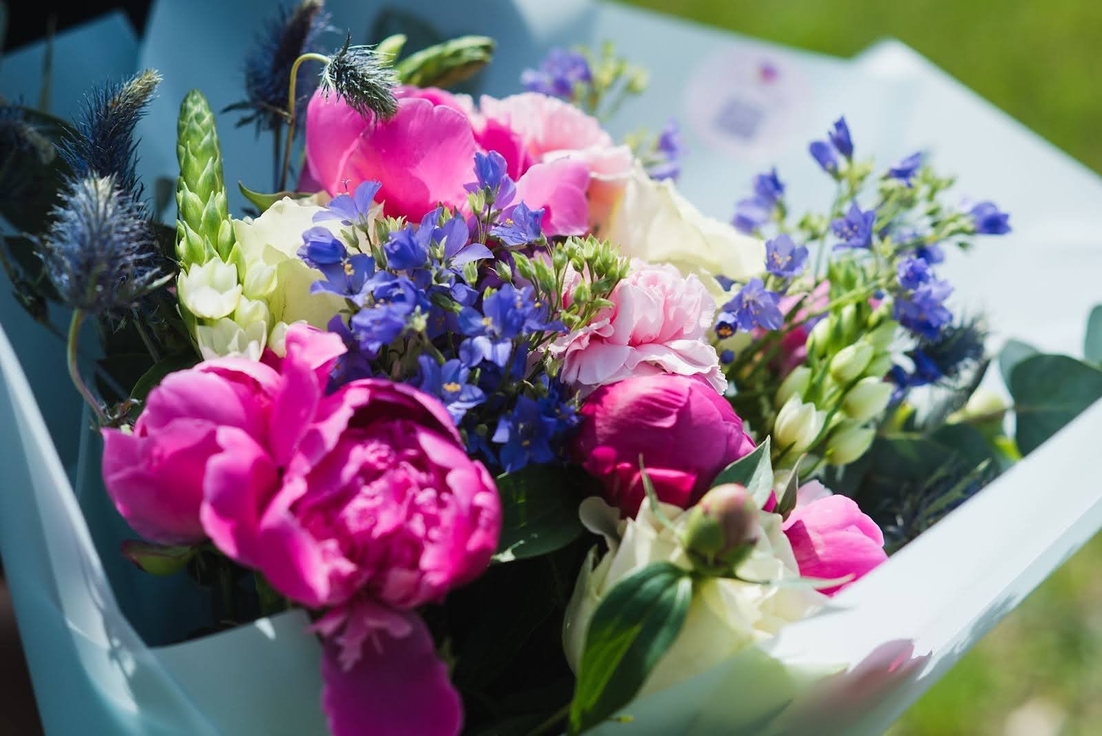 Bright summer bouquet featuring pink peonies, blue thistles, and purple wildflowers wrapped in paper