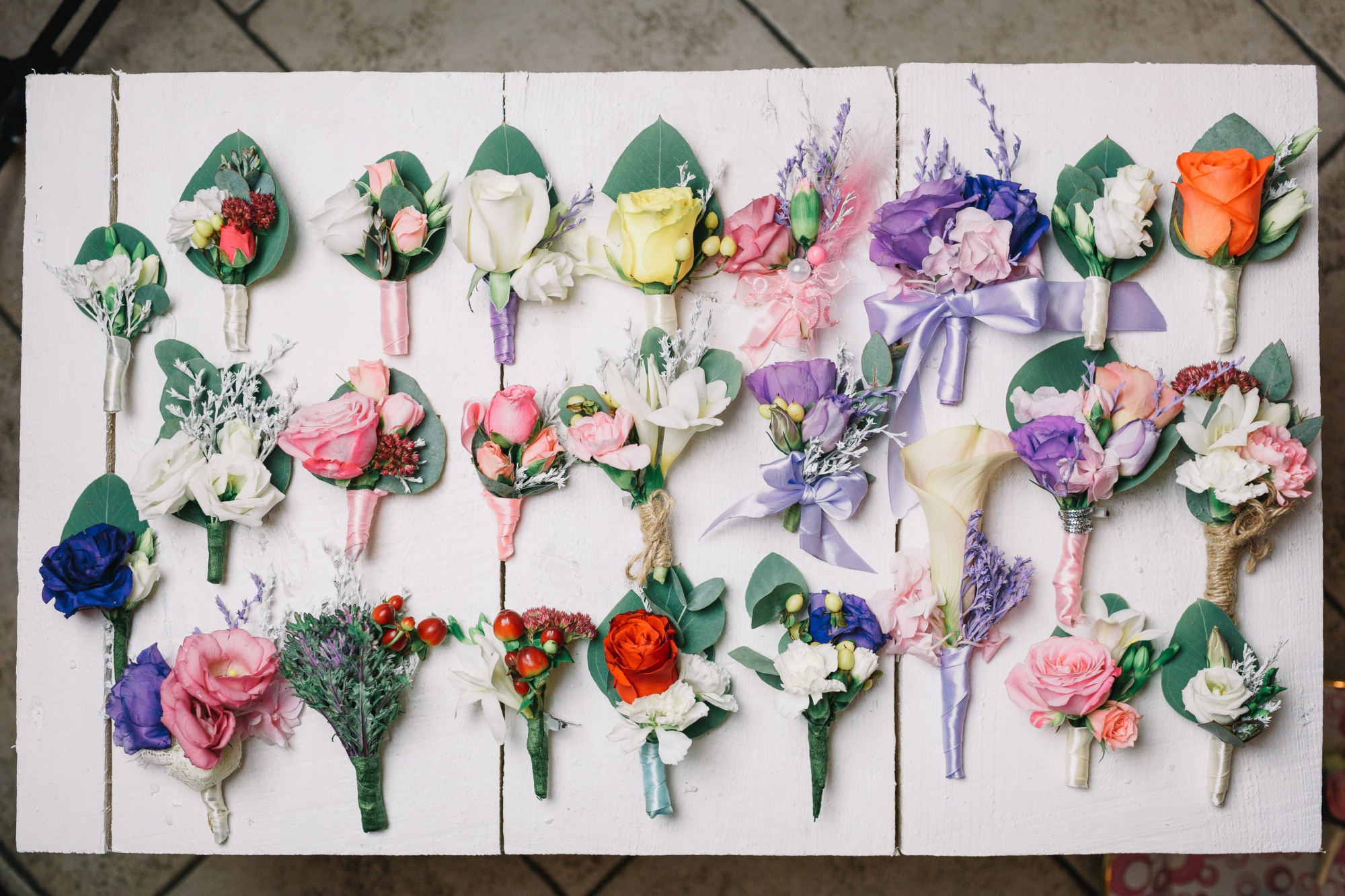 Variety of pin-on wedding corsages in different flowers, colours and ribbon styles laid on a white board